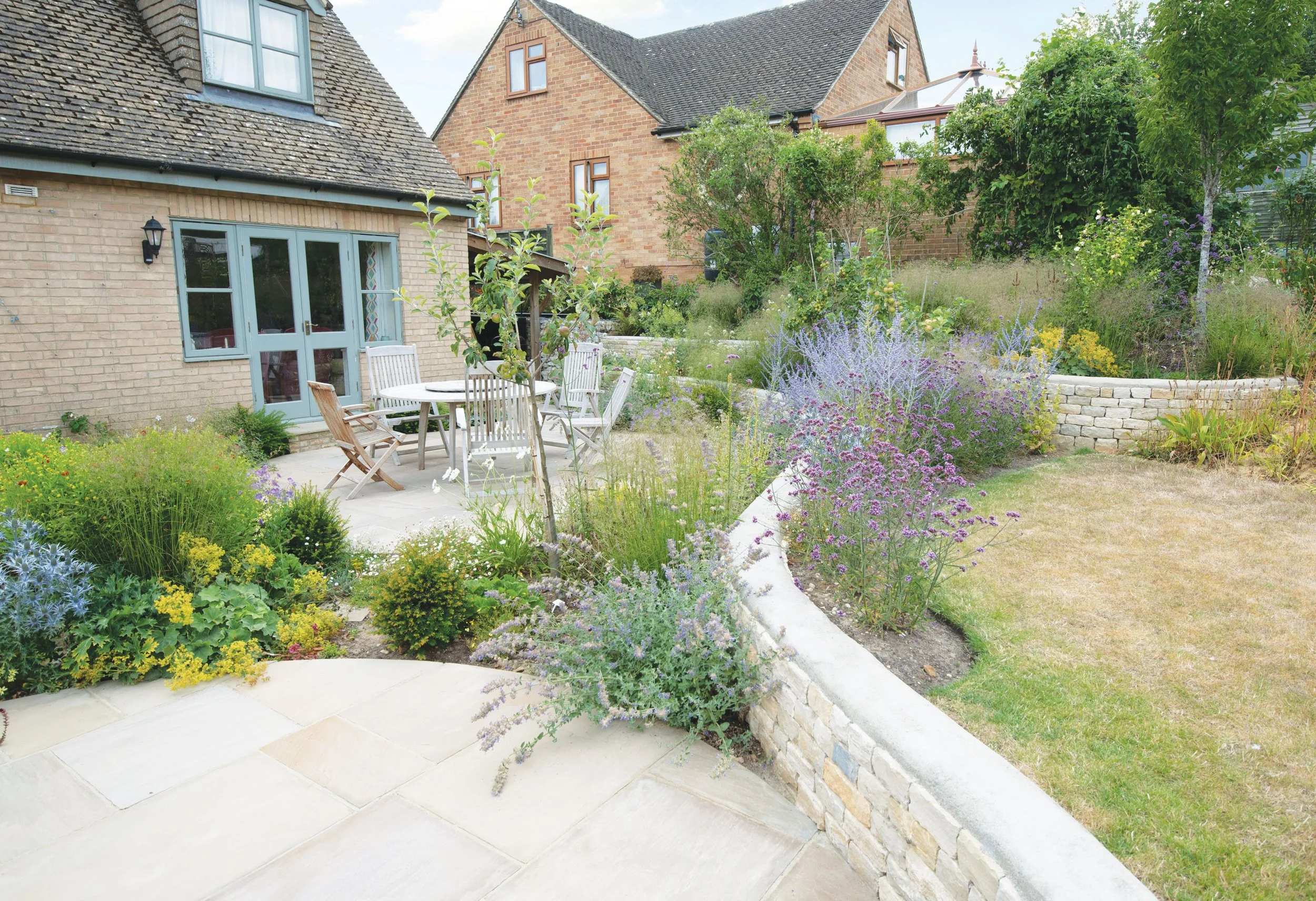 View from the house across the planted terraces, where curving stone walls lead into the looser landscape beyond.