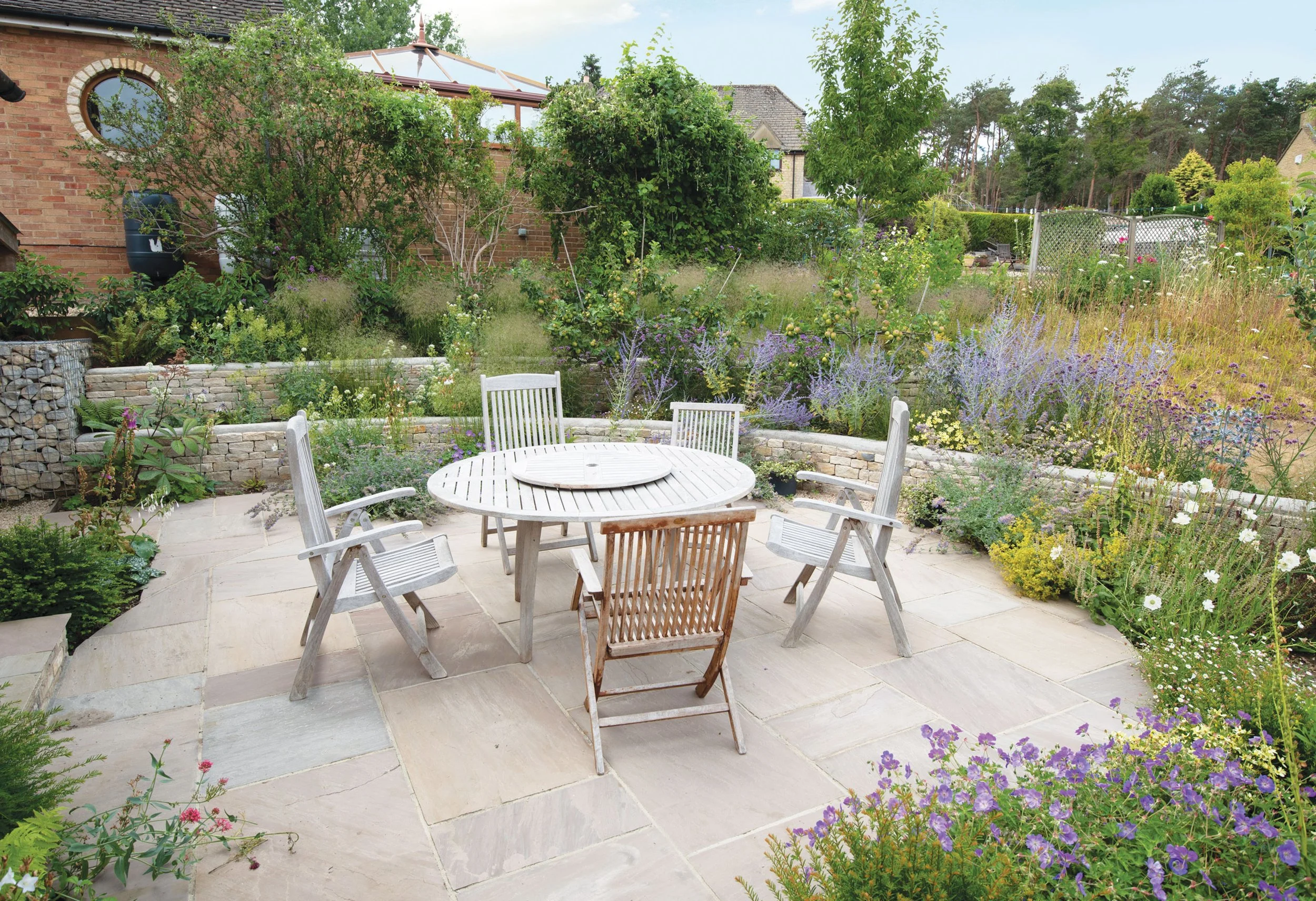 Circular family dining terrace enclosed by abundant perennial planting and curving dry-stone walls.