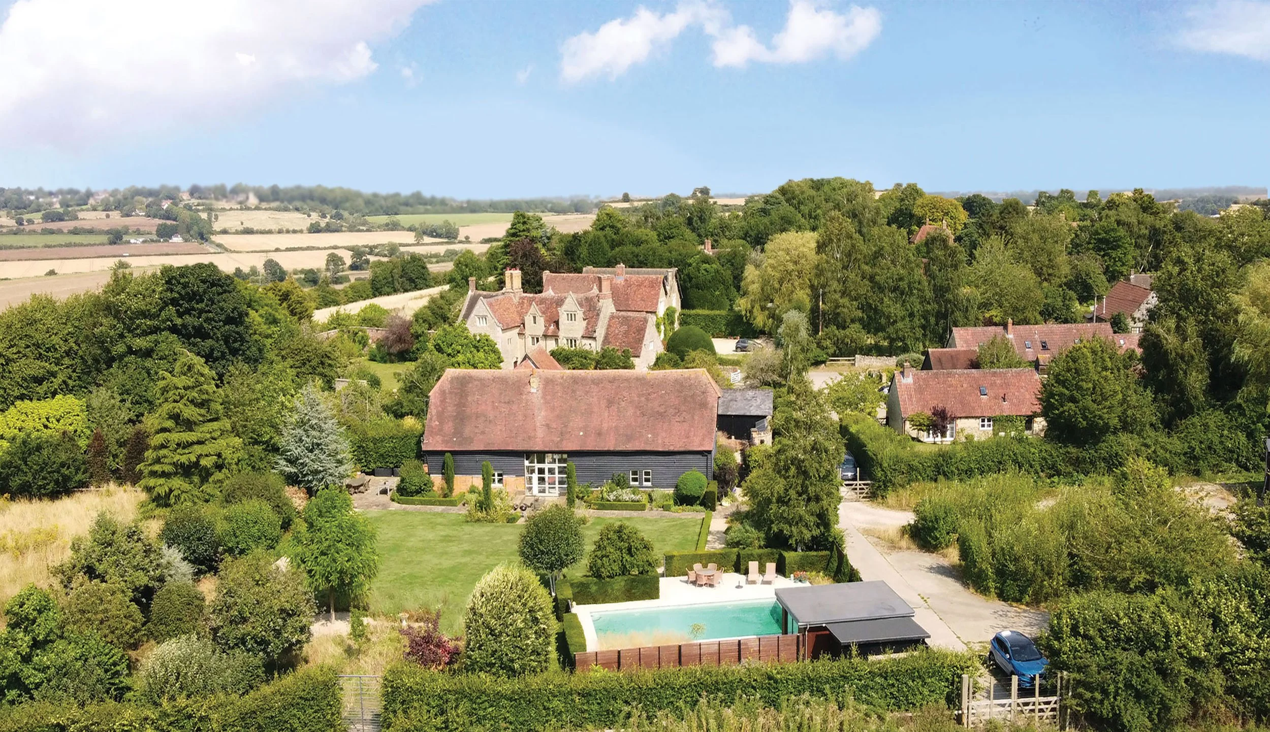 Aerial view of The Barn Garden in Toot Baldon Oxfordshire, showing the converted barn, courtyard garden, swimming pool and surrounding countryside.