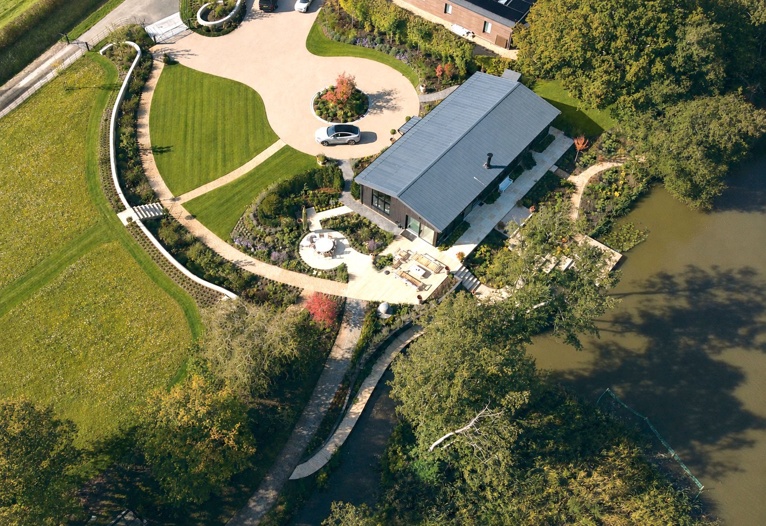 Aerial view of The Lake House showing the contemporary house, curved garden walls, lawns, planting and lake edge.