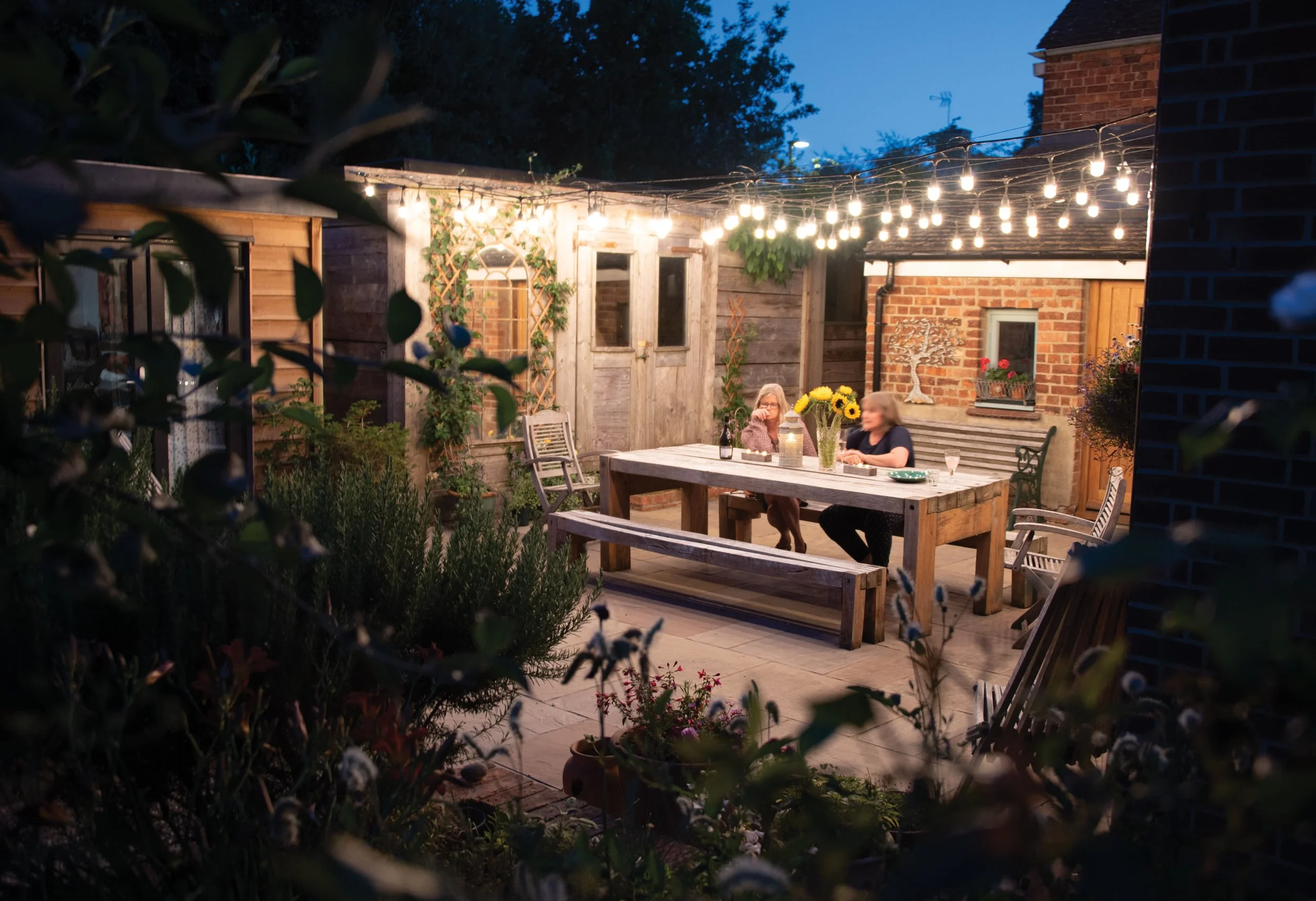 The Quad Garden at night, with festoon lighting creating a warm sense of enclosure around the courtyard seating area.