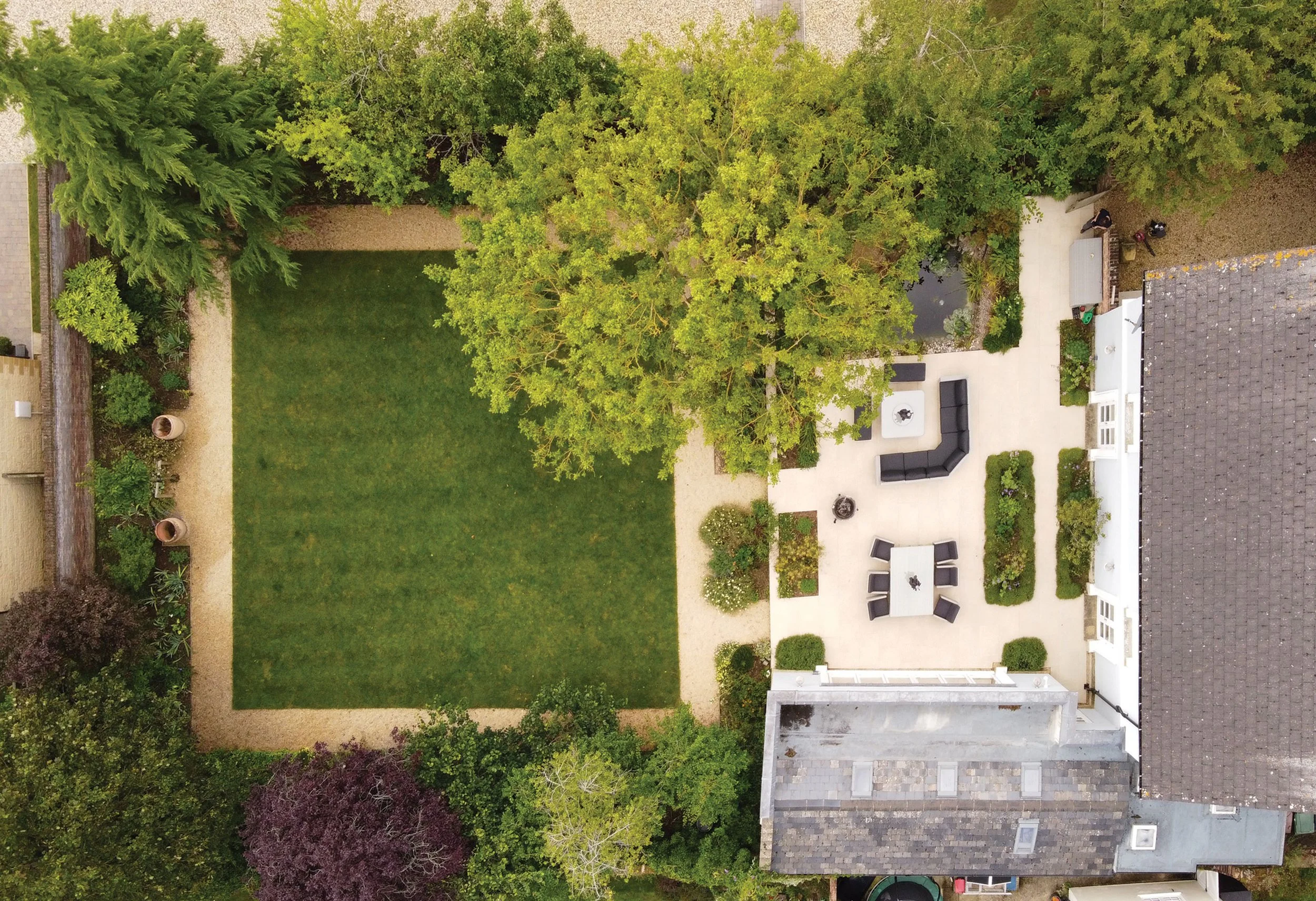 Aerial view of a formal garden with lawn, mature trees, paved terraces and structured planting around the house.