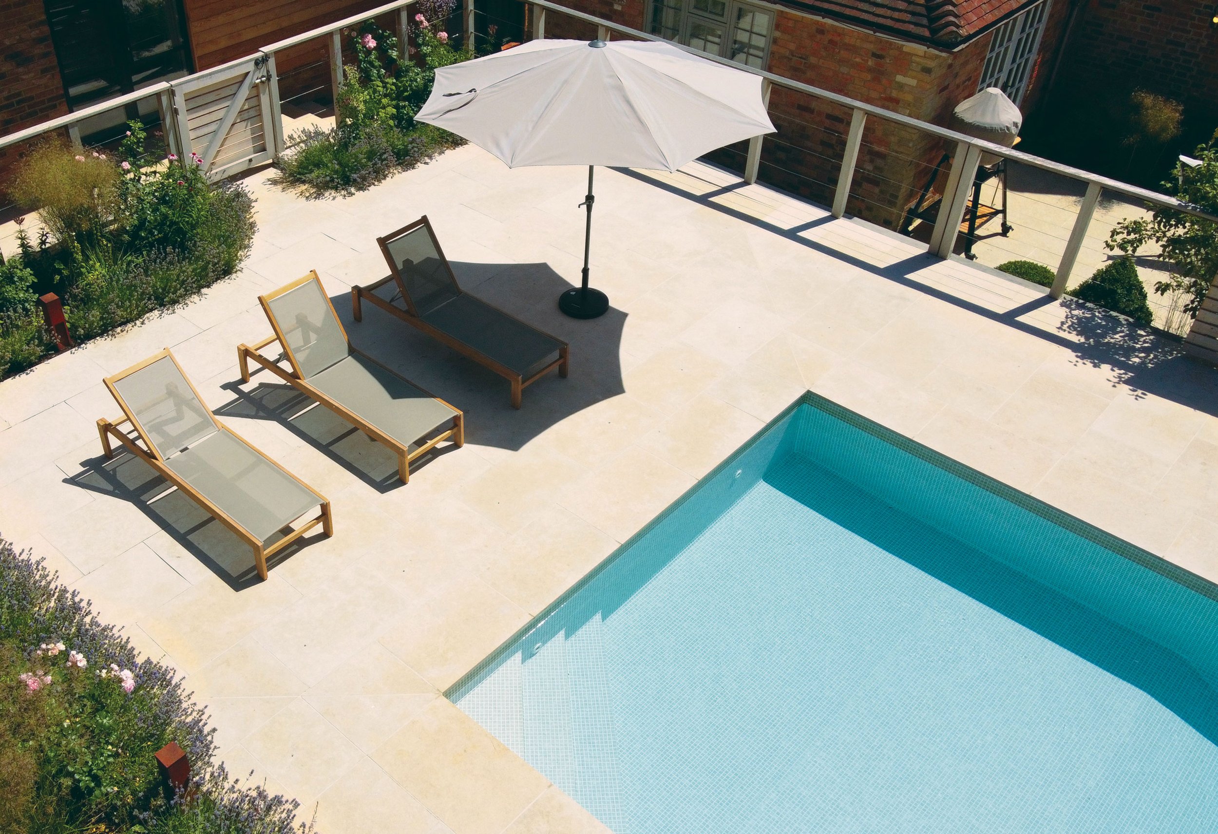 Pale stone pool terrace with family seating and loungers beside the redesigned swimming pool in Marsh Baldon.