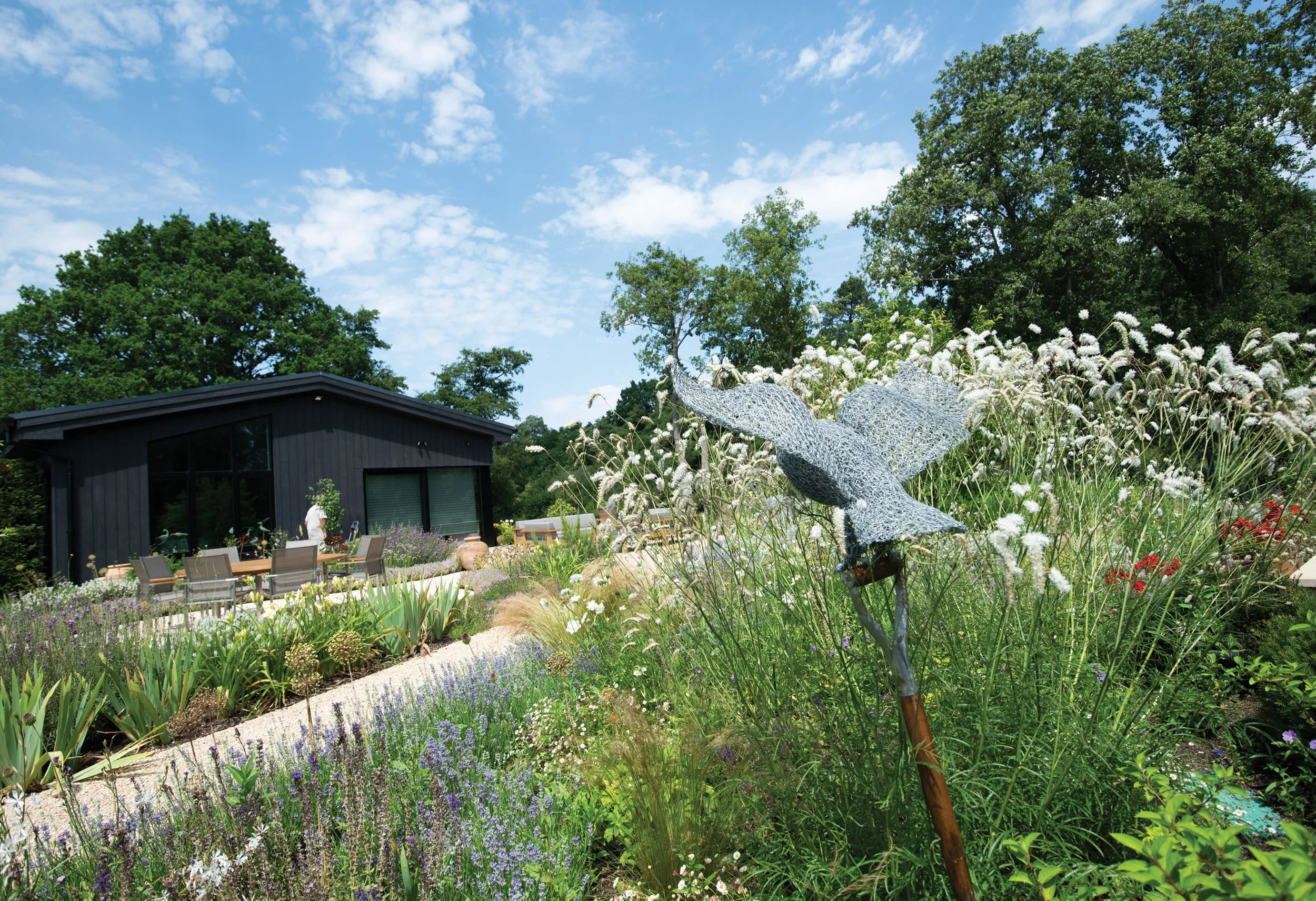 Layered perennial and grass planting beside the contemporary house, designed to soften the transition into the surrounding landscape, owl sculpture shown.