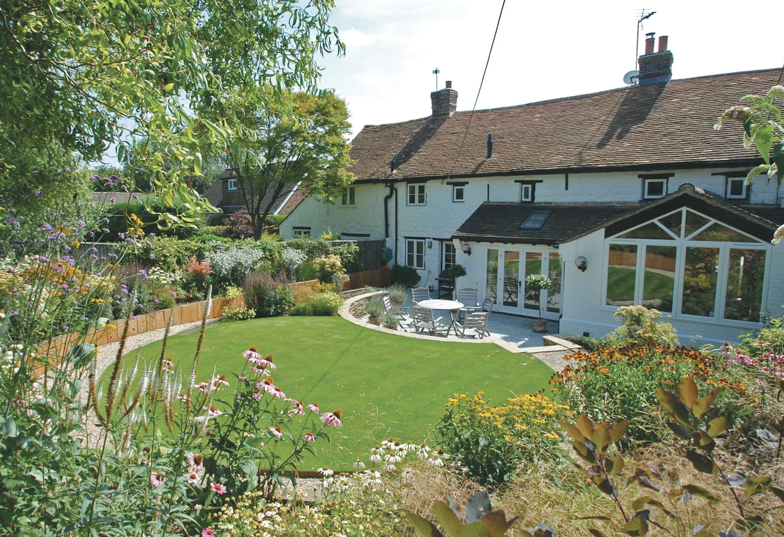 Family garden with curved lawn and richly planted borders connecting the house with the wider garden.