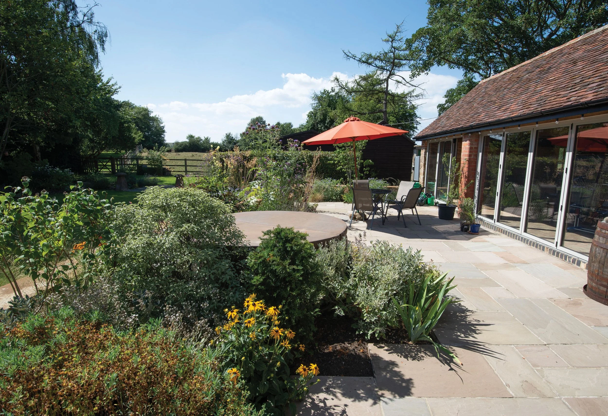 Courtyard terrace and entertaining space surrounded by relaxed perennial planting beside the converted barn.