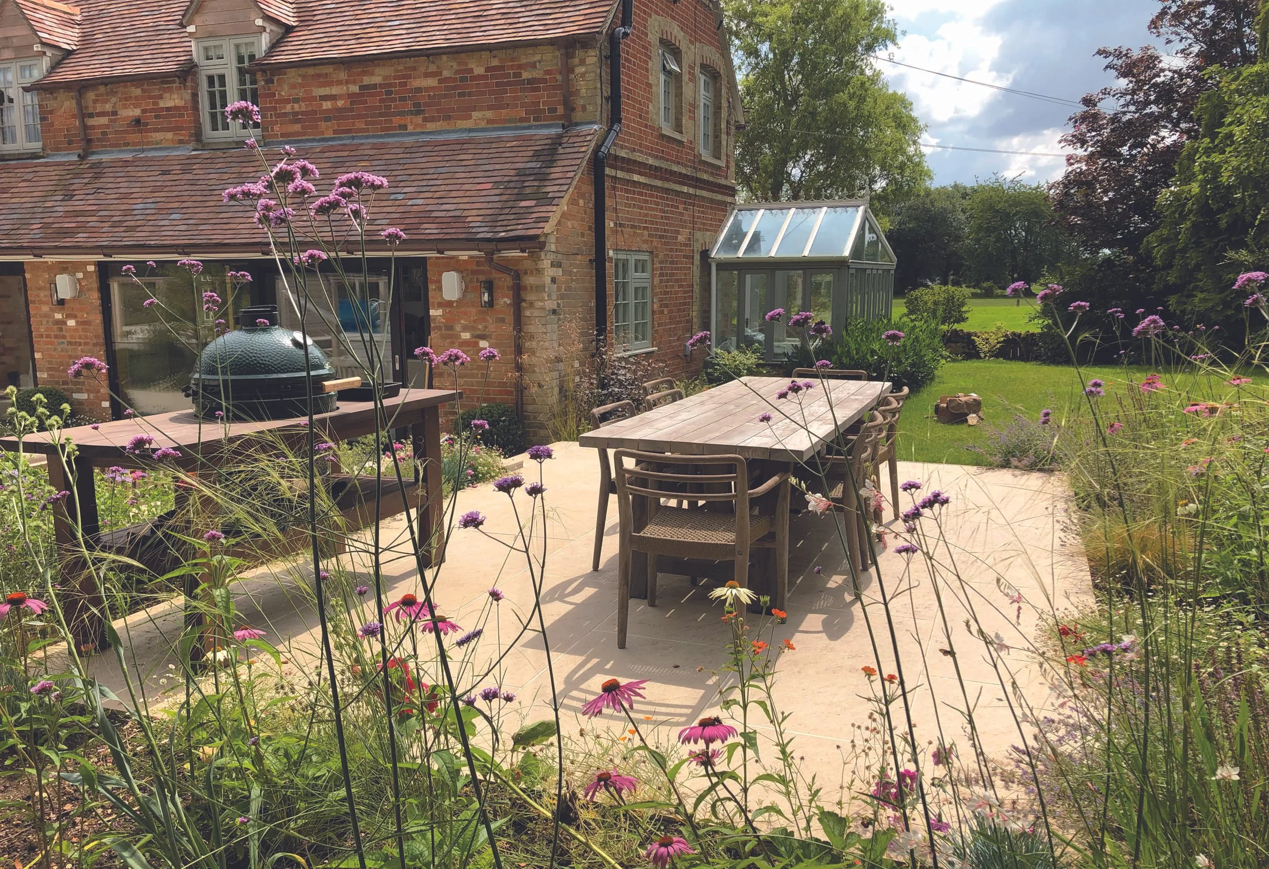 Family dining terrace beside the renovated Oxfordshire house, softened by Verbena and informal perennial planting.