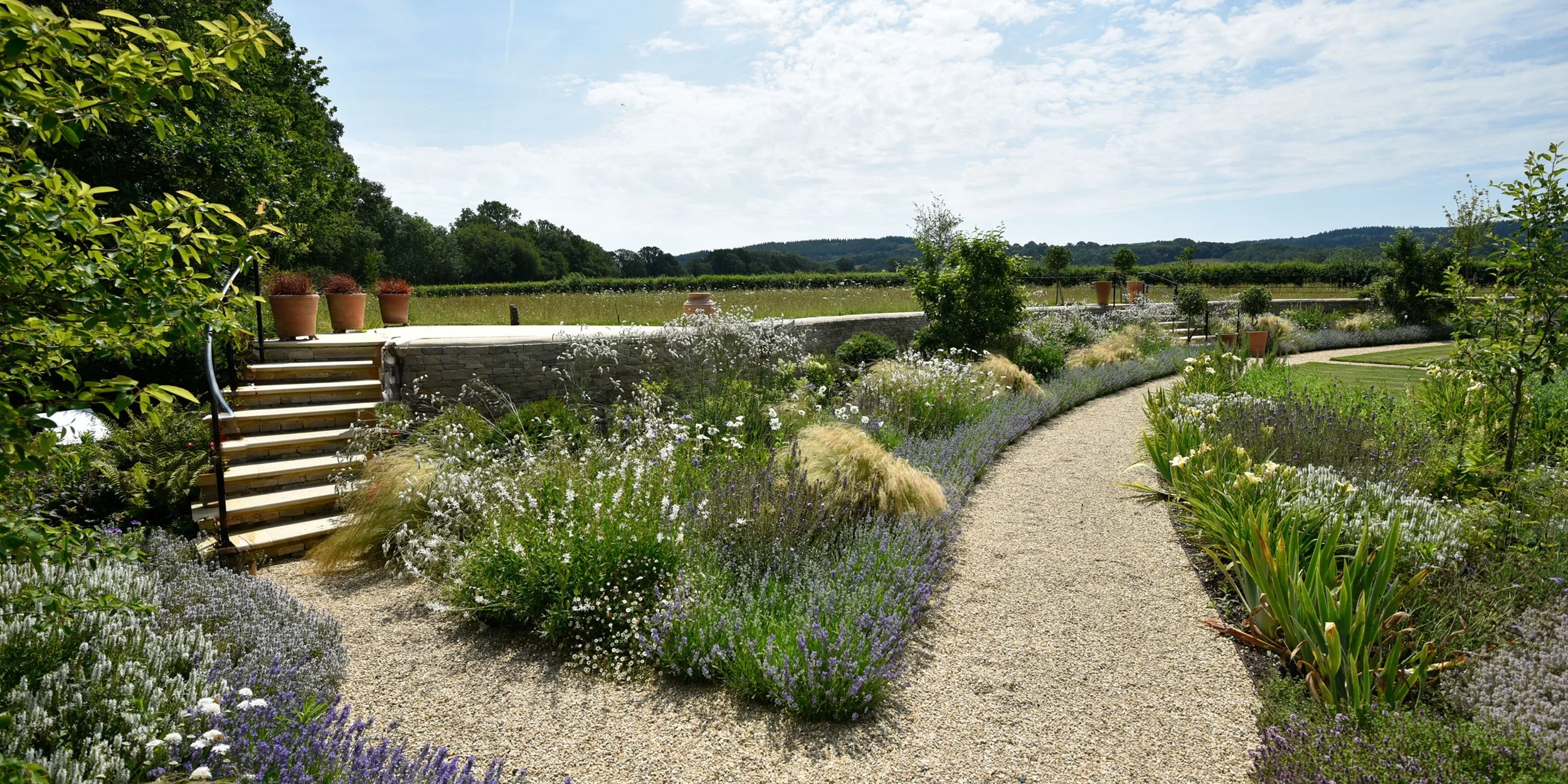 Curving gravel path beside a stone wall and naturalistic planting in a contemporary country garden by Doug Holloway Landscape Design.”