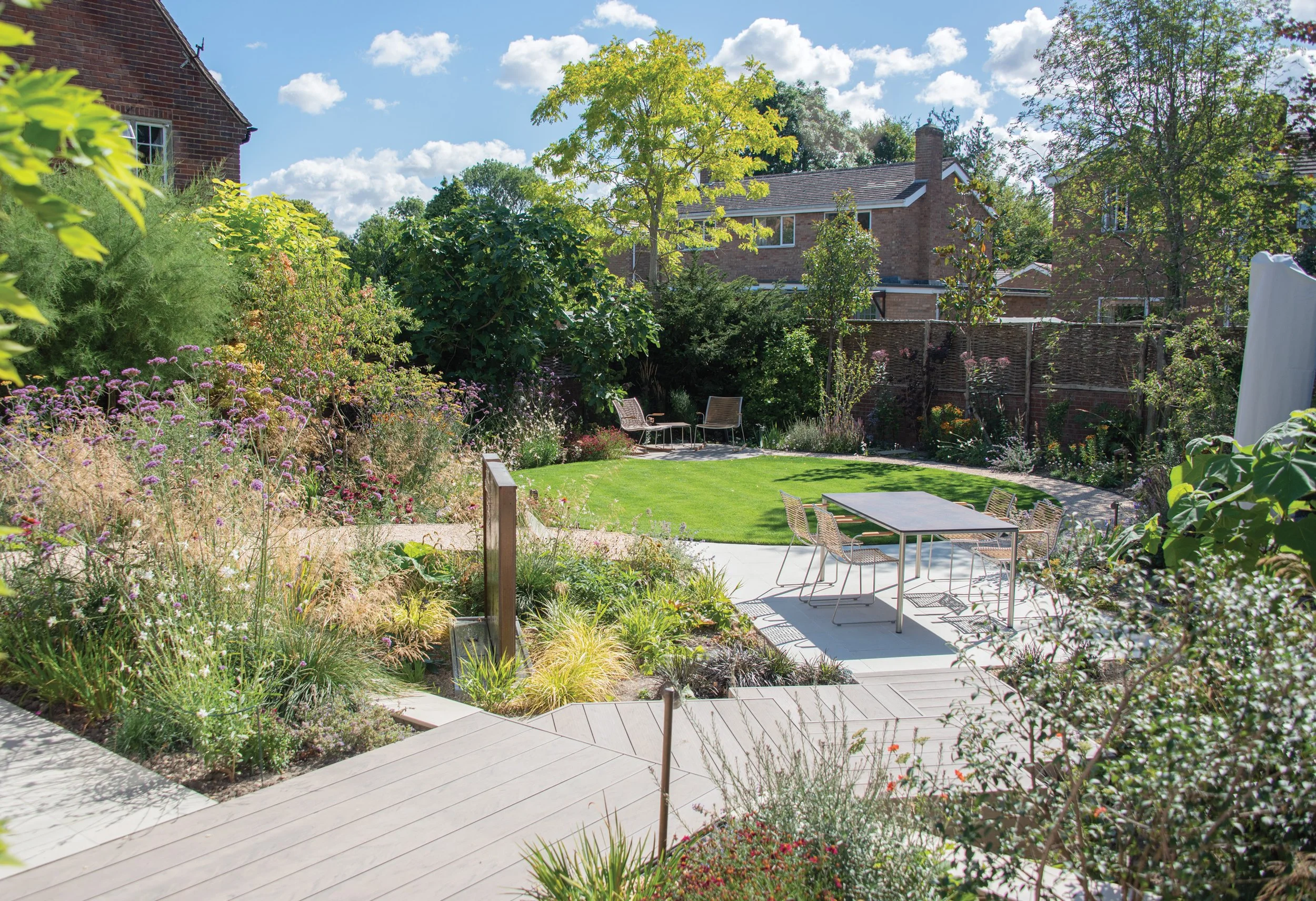 Contemporary garden with composite decking, gravel paths and naturalistic planting arranged around a small lawn.