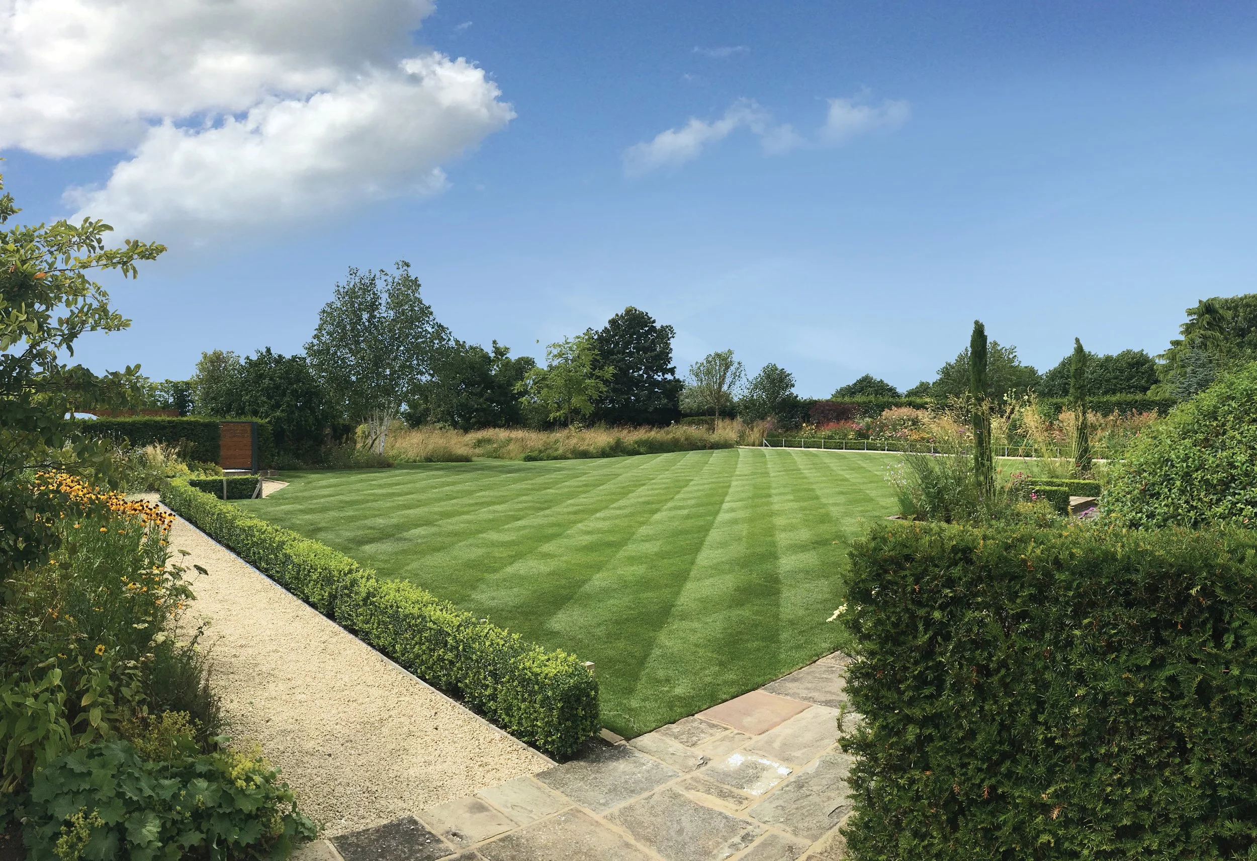 Rear garden with an expansive family lawn, low clipped hedges and planted borders designed to accommodate children playing football.
