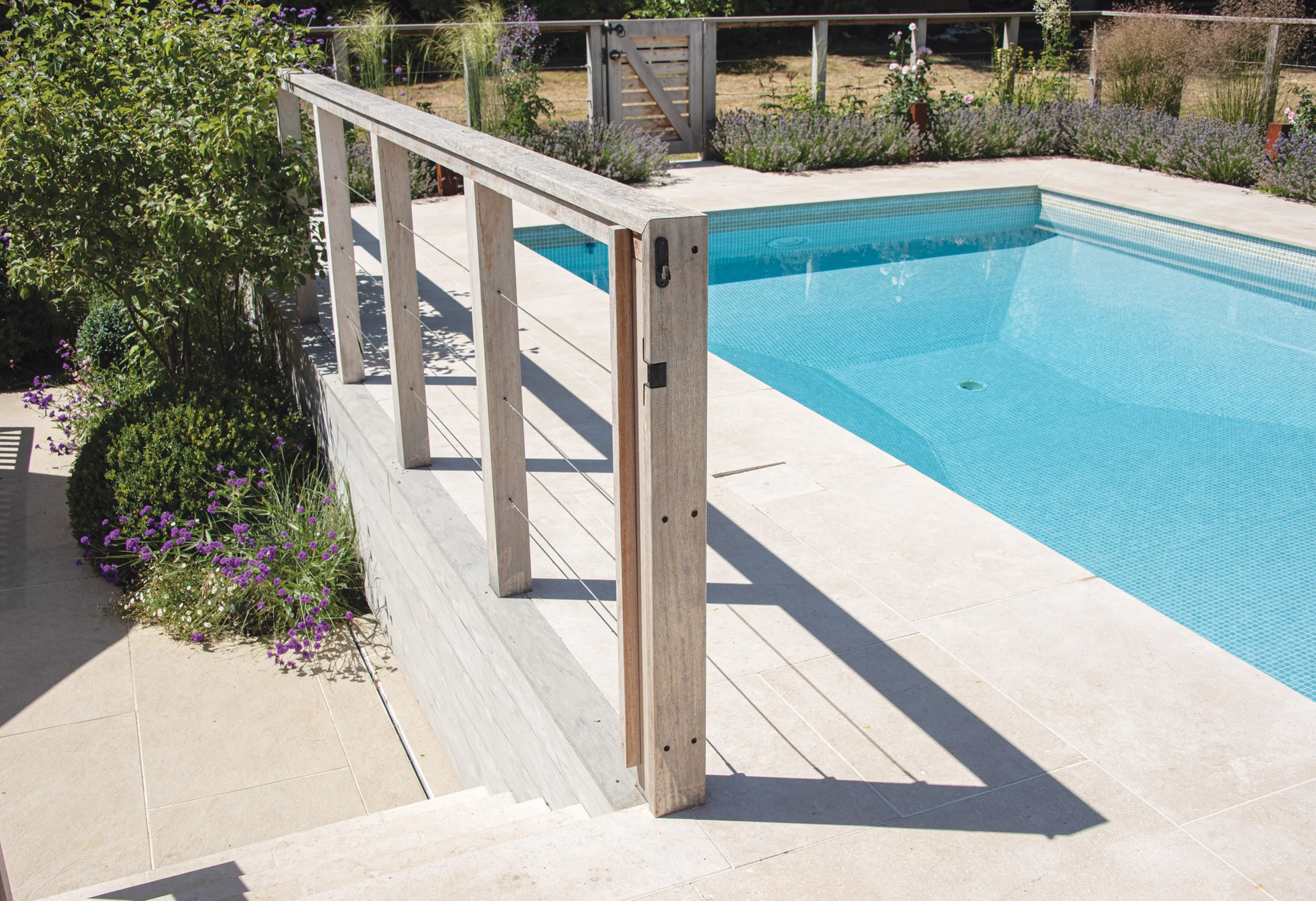 Detail of the redesigned swimming pool enclosure with timber balustrade, pale stone steps and surrounding planting.