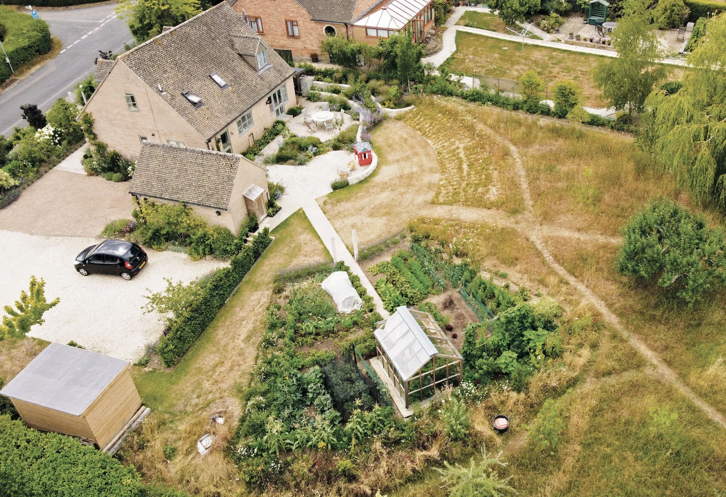 Aerial view of The Kitchen Garden in Finstock, Oxfordshire, showing the curving terraces, productive garden, greenhouse, meadow and fruit trees.