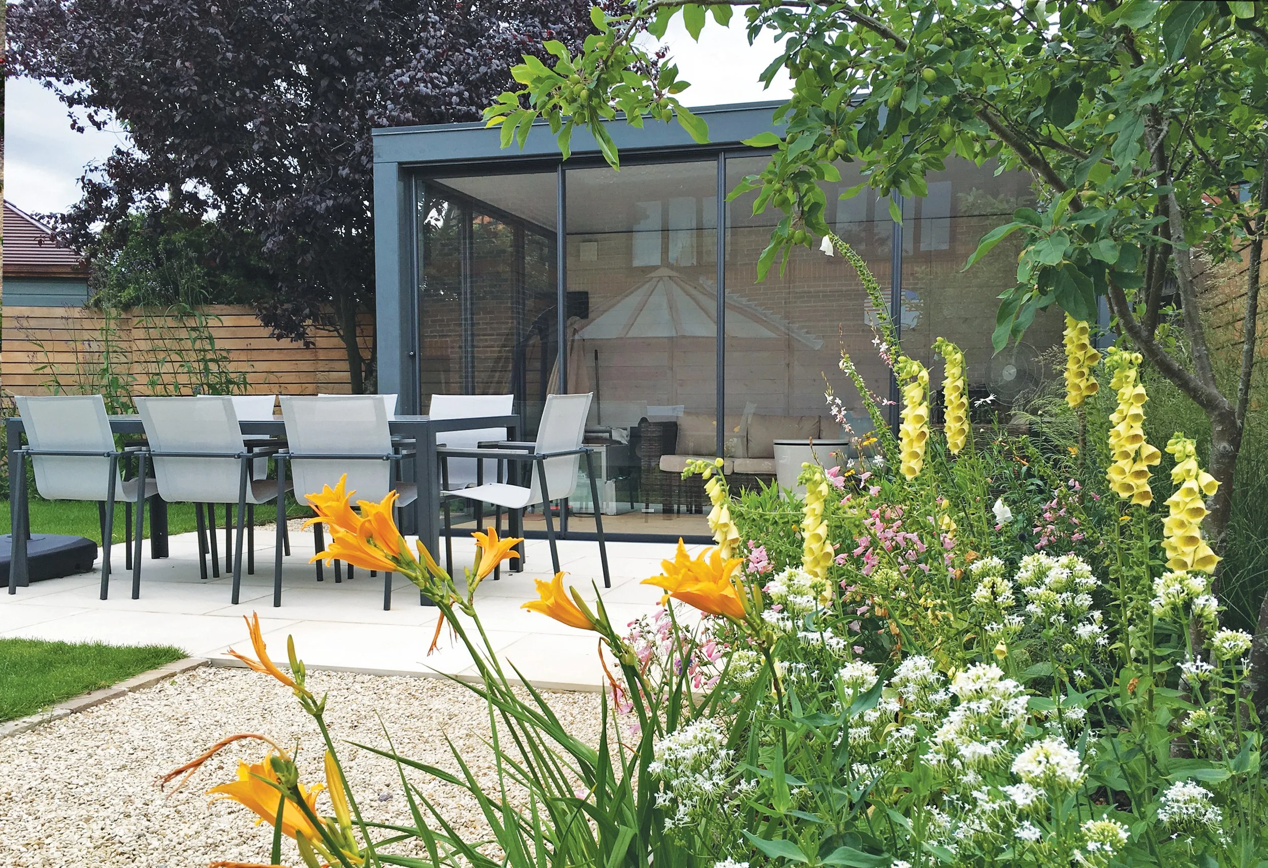 Contemporary garden building and dining terrace surrounded by colourful perennial planting and gravel paths.