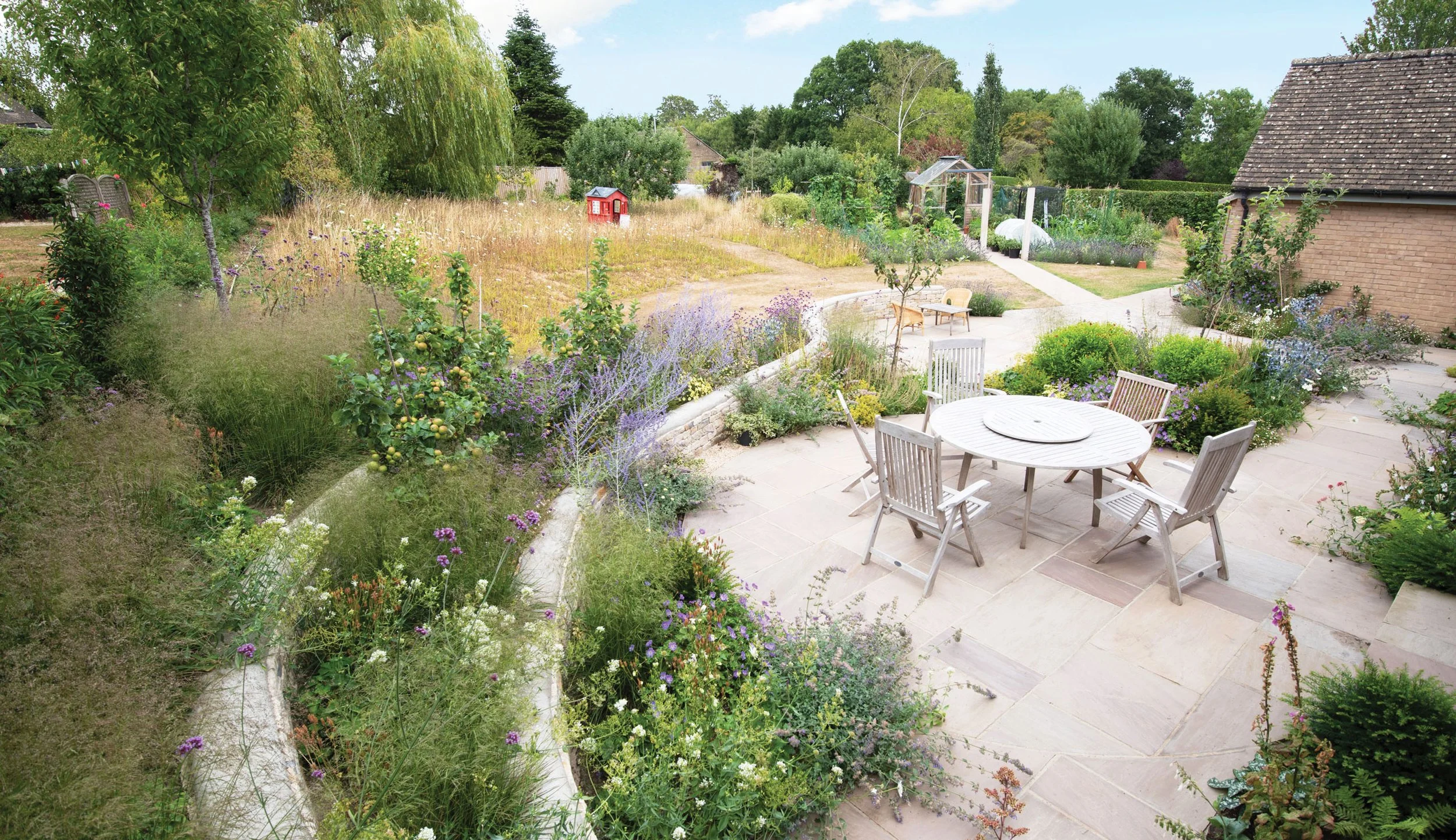 Curved dry-stone retaining walls creating layered planting beds, with perennials spilling over the different levels beside the main terrace.