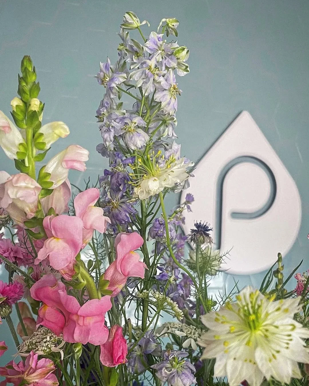 Colorful bouquet of pink, purple, white, and cream flowers with a white house-shaped decor piece in the background.