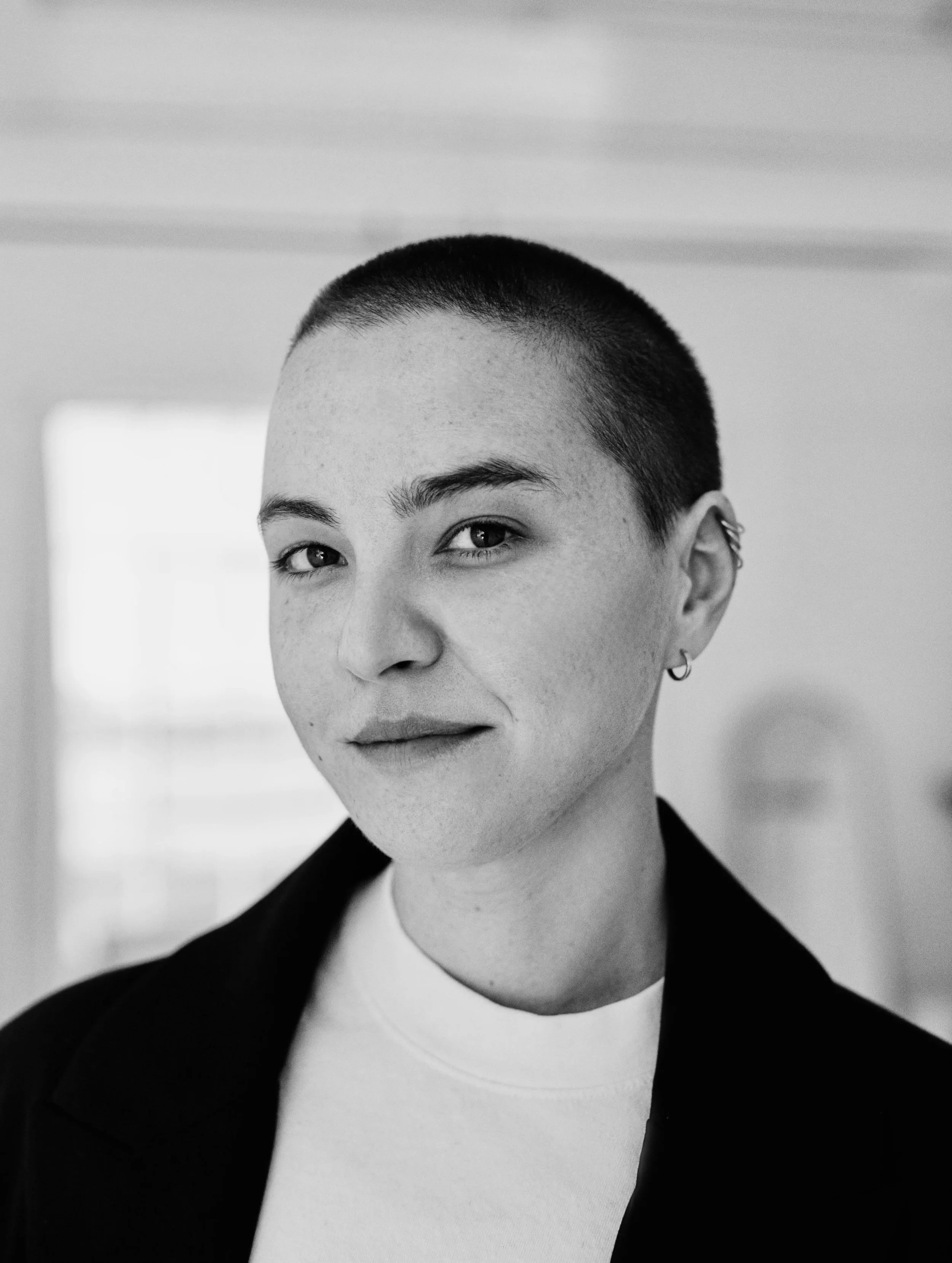 Black and white portrait of a woman with short hair, wearing a white shirt and black blazer, looking at the camera with a slight smile.