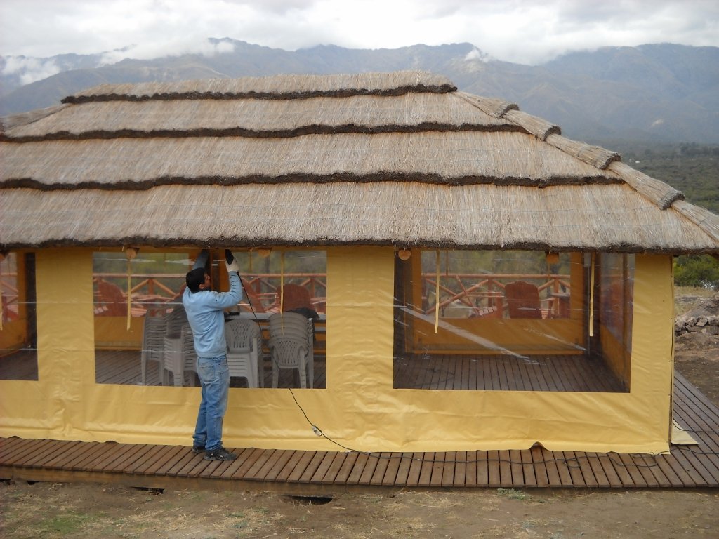 Instalación de cerramiento tipo cortina levadiza en quincho. Operario colocando lona cristal a medida. Fabricación y envío de cerramientos en San Luis.