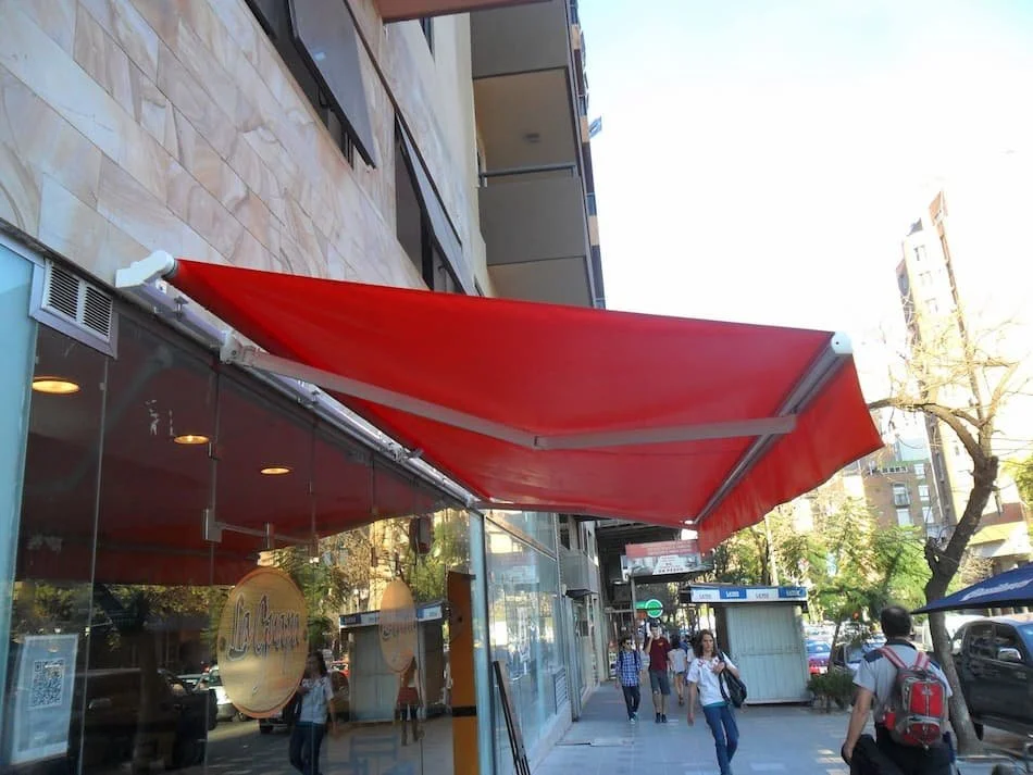 Toldo brazo invisible instalado en frente de local comercial, lona de PVC naranja, uso exterior.