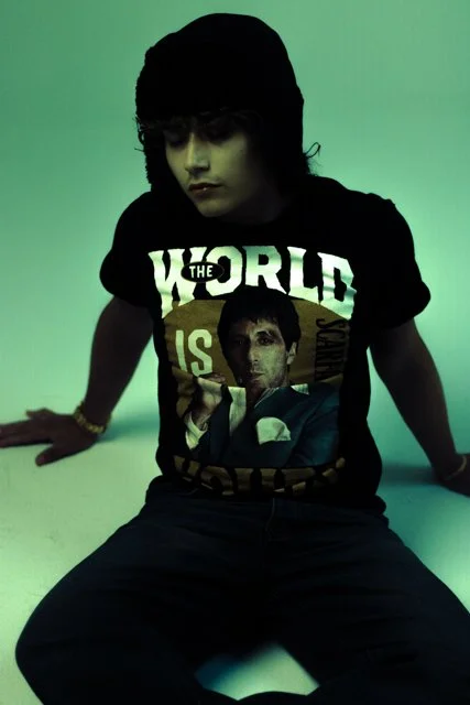 Person wearing a black t-shirt with a graphic of a man holding a cigarette, sitting against a green background.