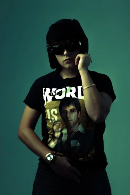 Person wearing black sunglasses and a black t-shirt with a graphic of a man, standing against a plain background.
