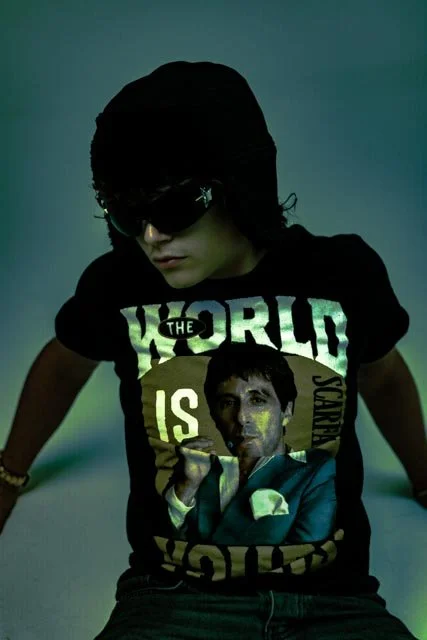 Person wearing sunglasses and a black T-shirt with a graphic of a man in a suit and text that says 'The World is Yours'.