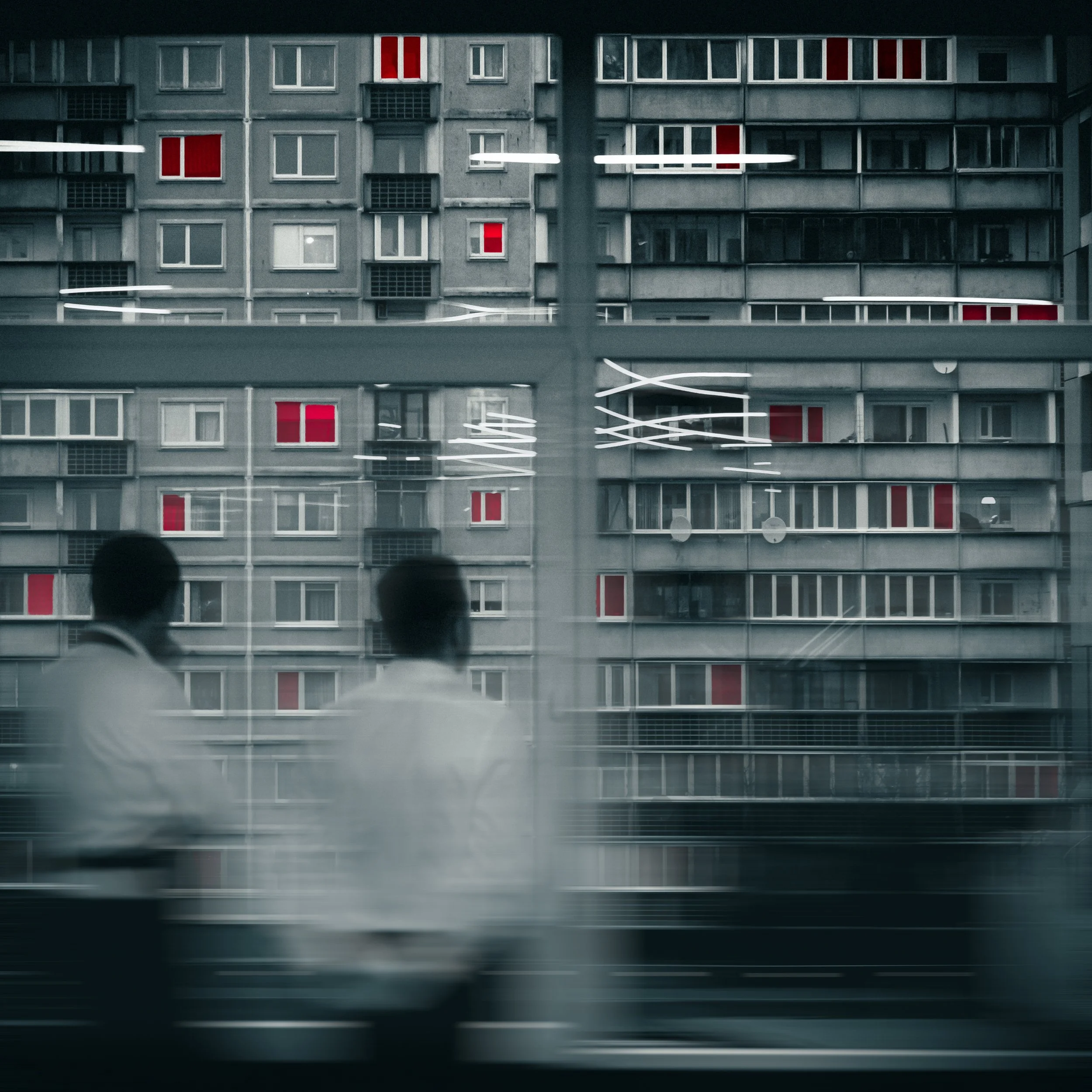 The image shows the reflection of a building with multiple windows and red-colored interior blinds in a glass window, with blurred silhouettes of two people at the bottom.