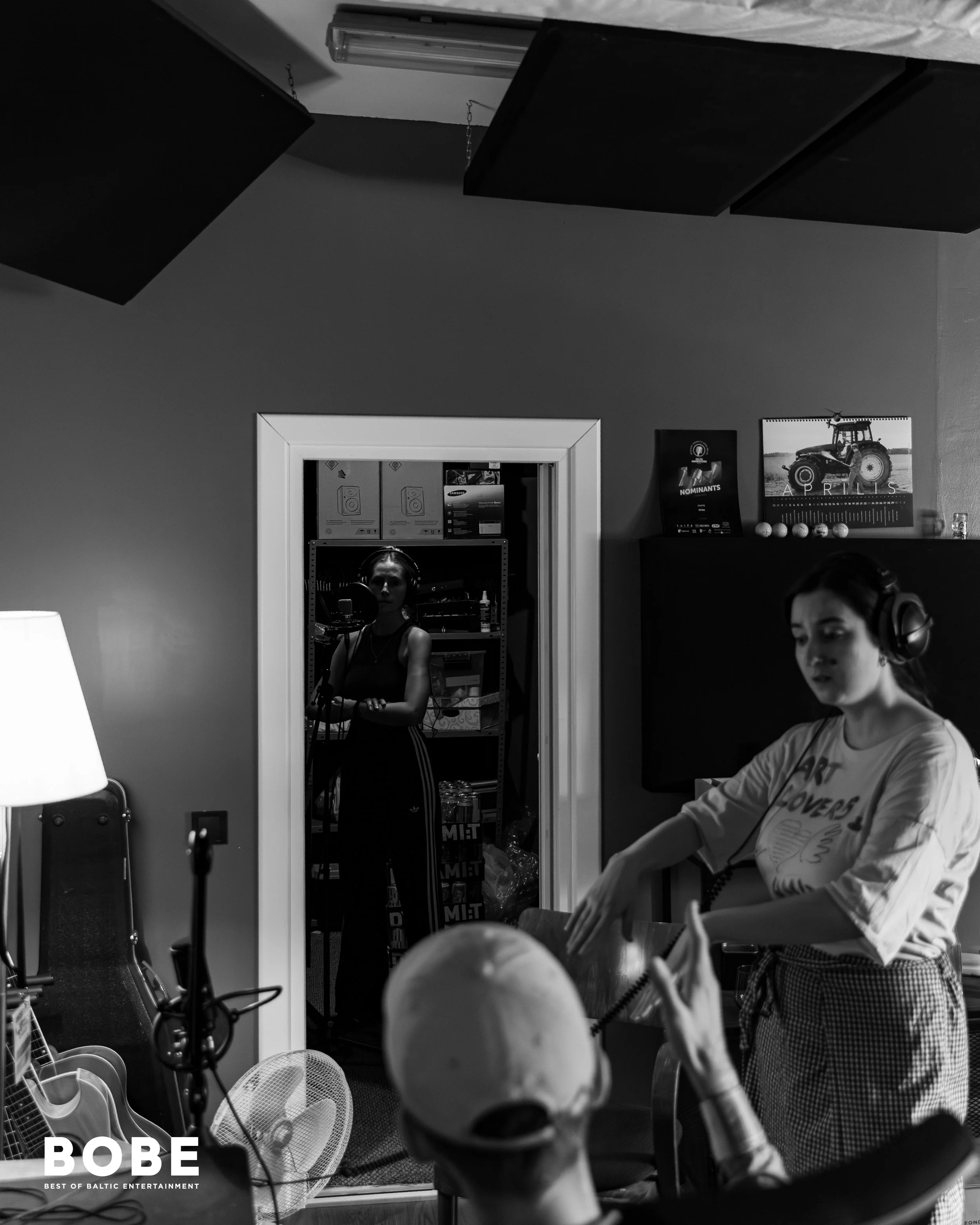 People sitting in a room with a mirror, musical instruments, and promotional posters on the walls.