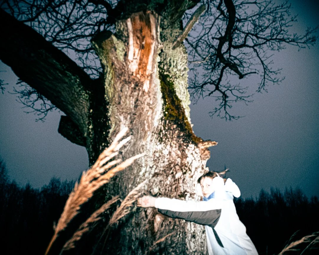 Person hugging a large, old tree at night in a wooded area.