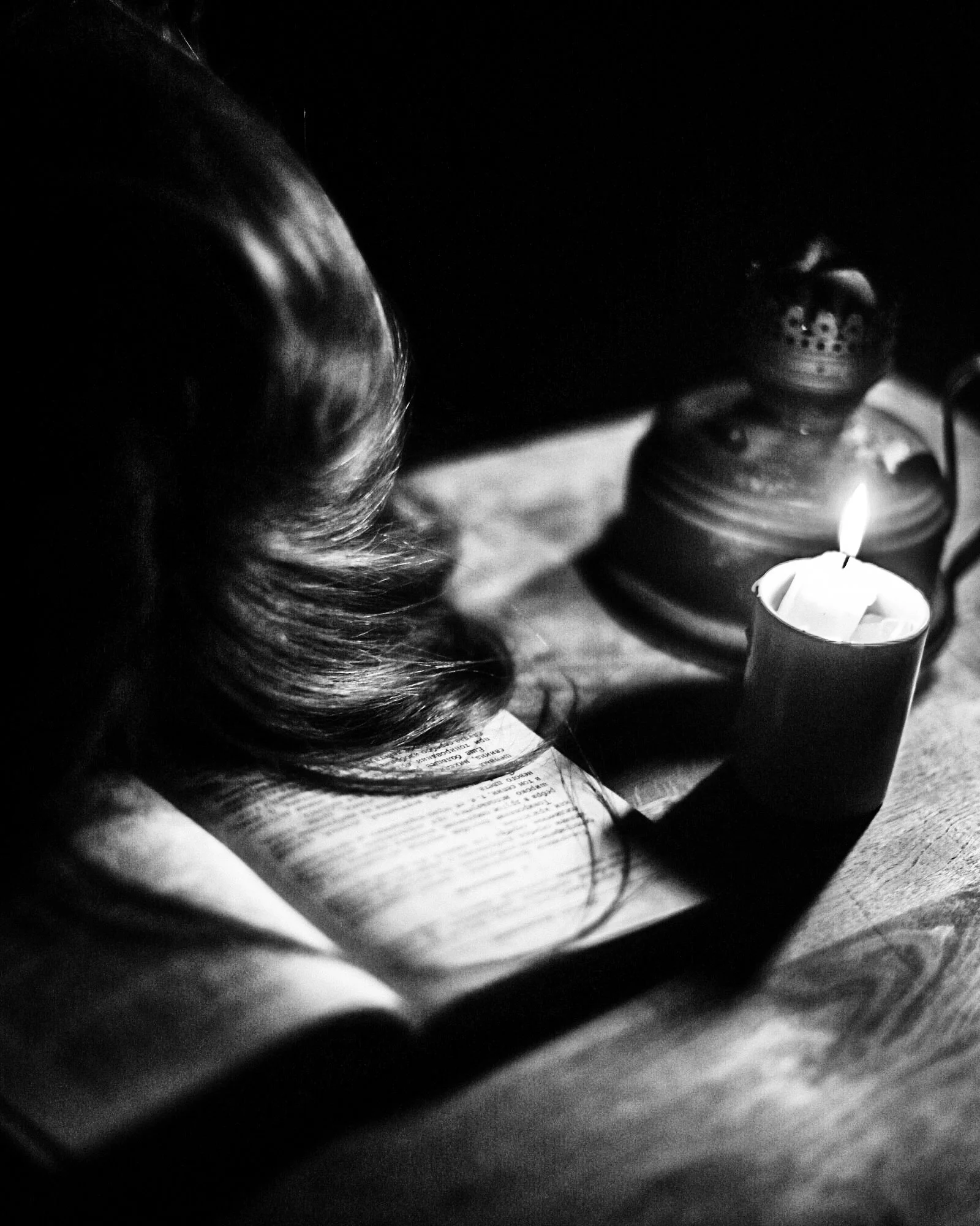 A person reading a book in a dimly lit room with a lit candle nearby.