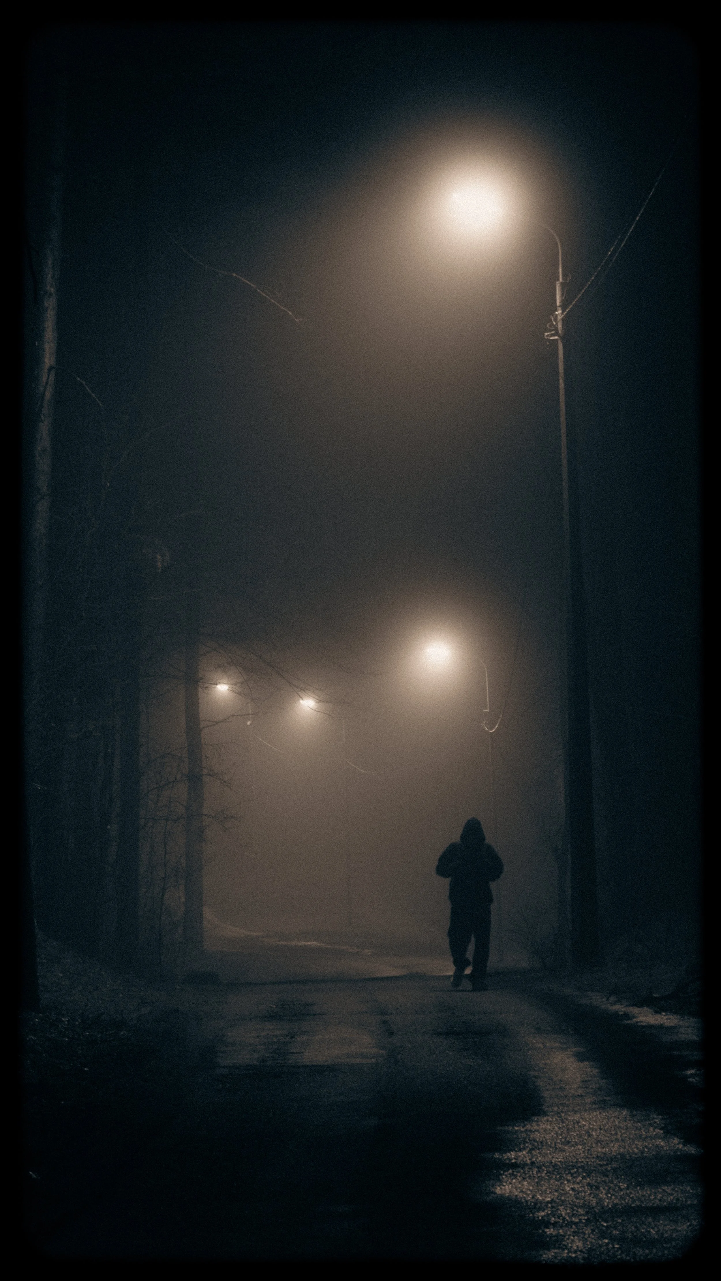 A person walking on a foggy street at night, illuminated by streetlights.