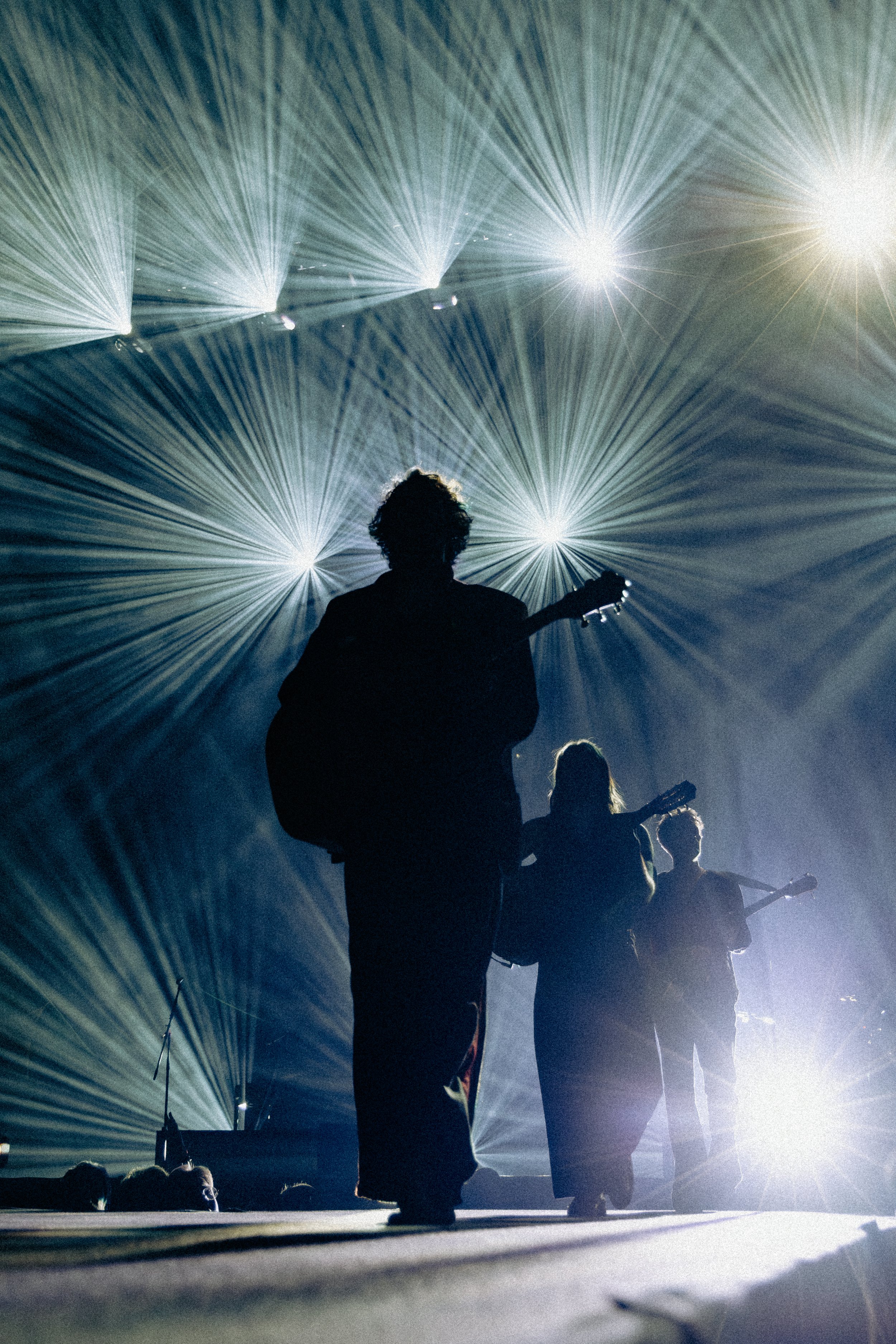 Silhouettes of musicians playing guitars on stage with dramatic lighting and laser effects.