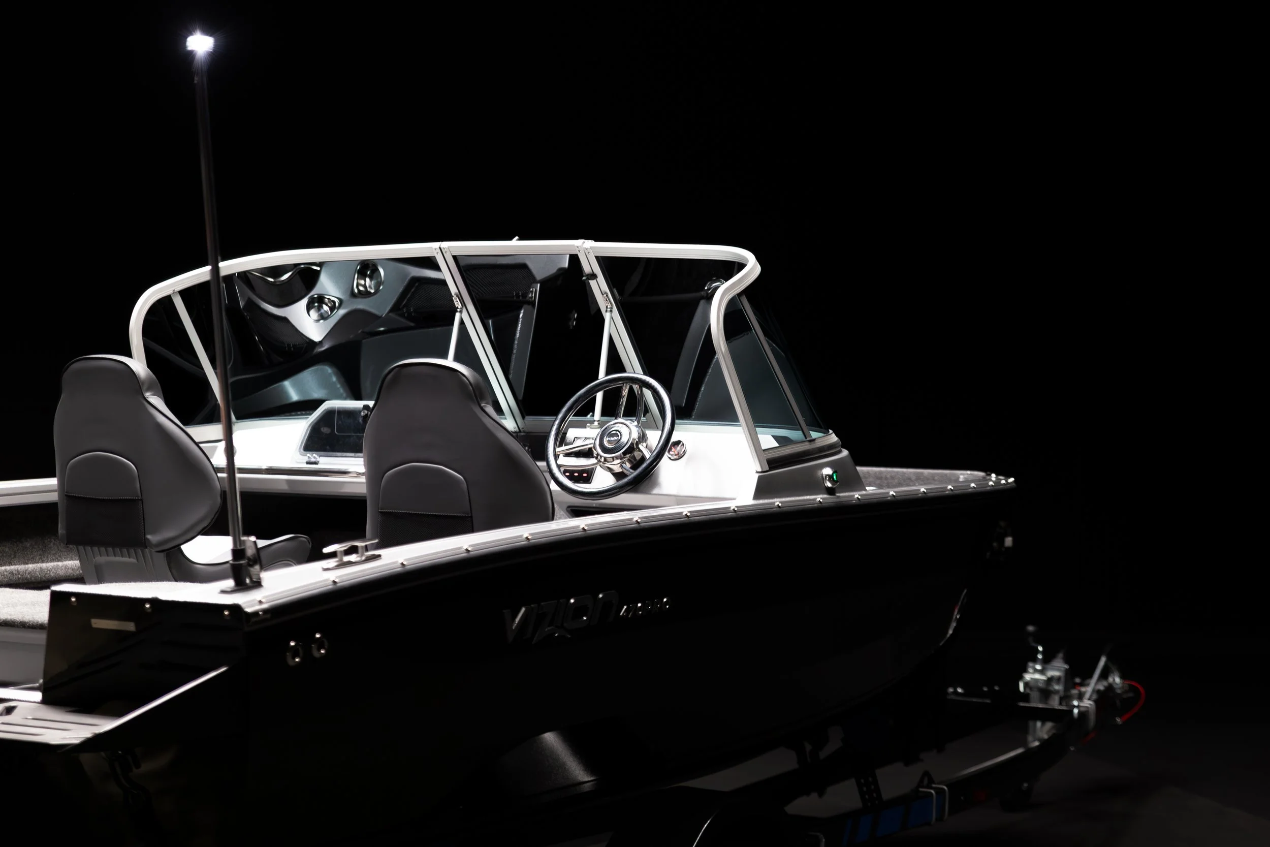A black and white boat with a steering wheel and seats, equipped with a tall light pole, displayed against a black background.