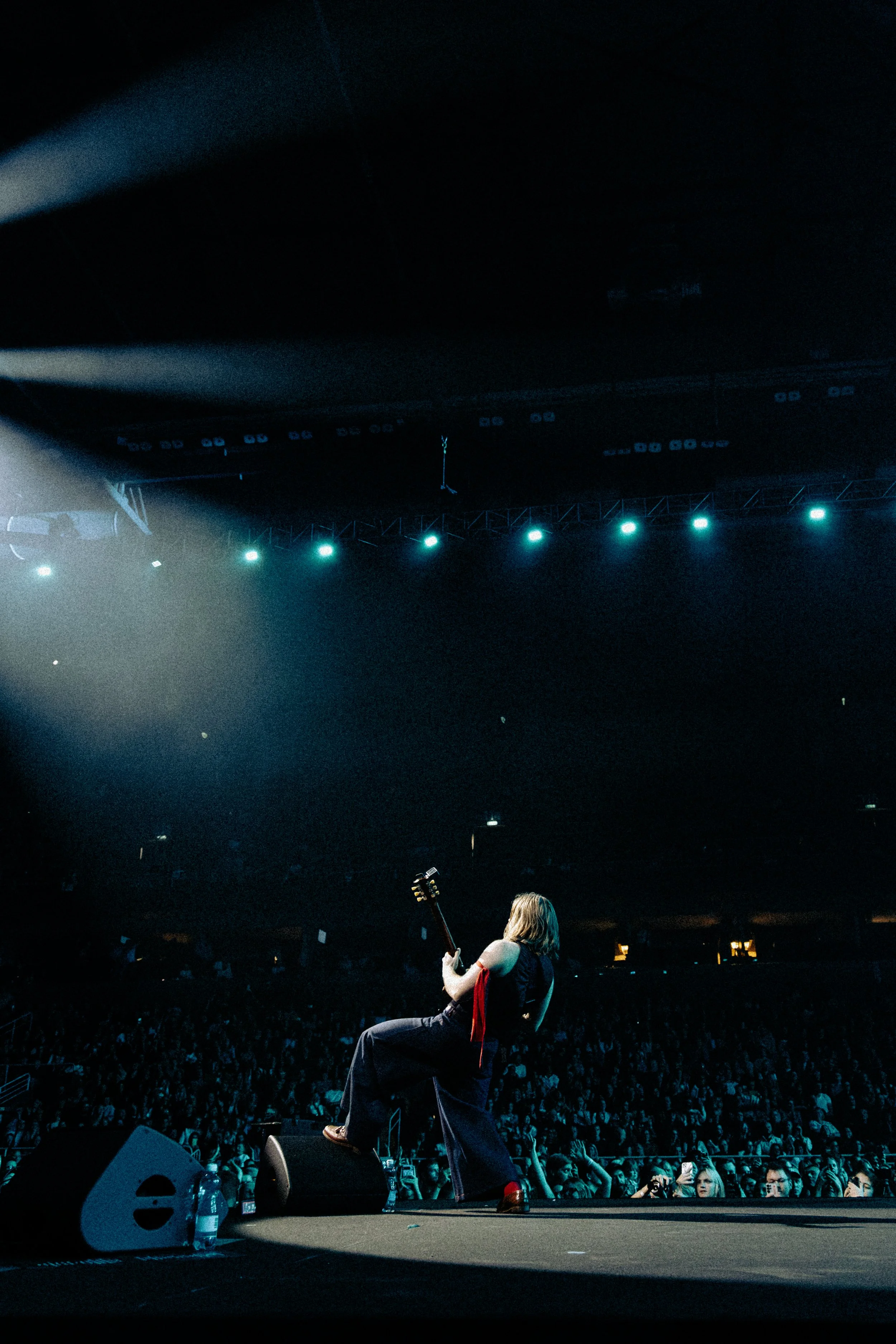 A musician playing an electric guitar on stage during a concert with an audience watching.