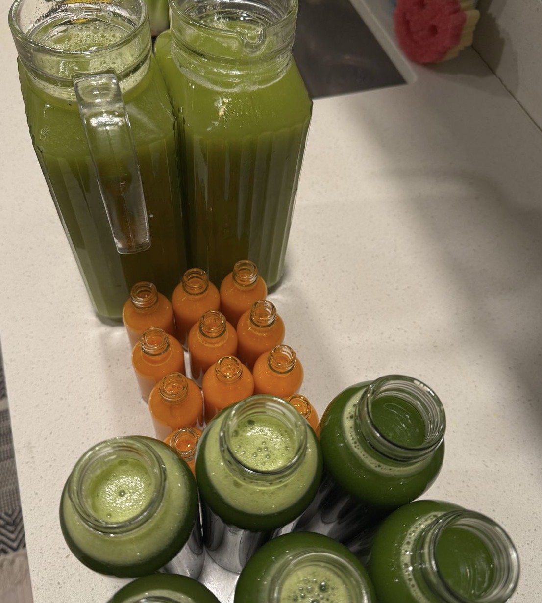Several green and orange juice bottles on a kitchen counter with some empty glass bottles surrounding them.