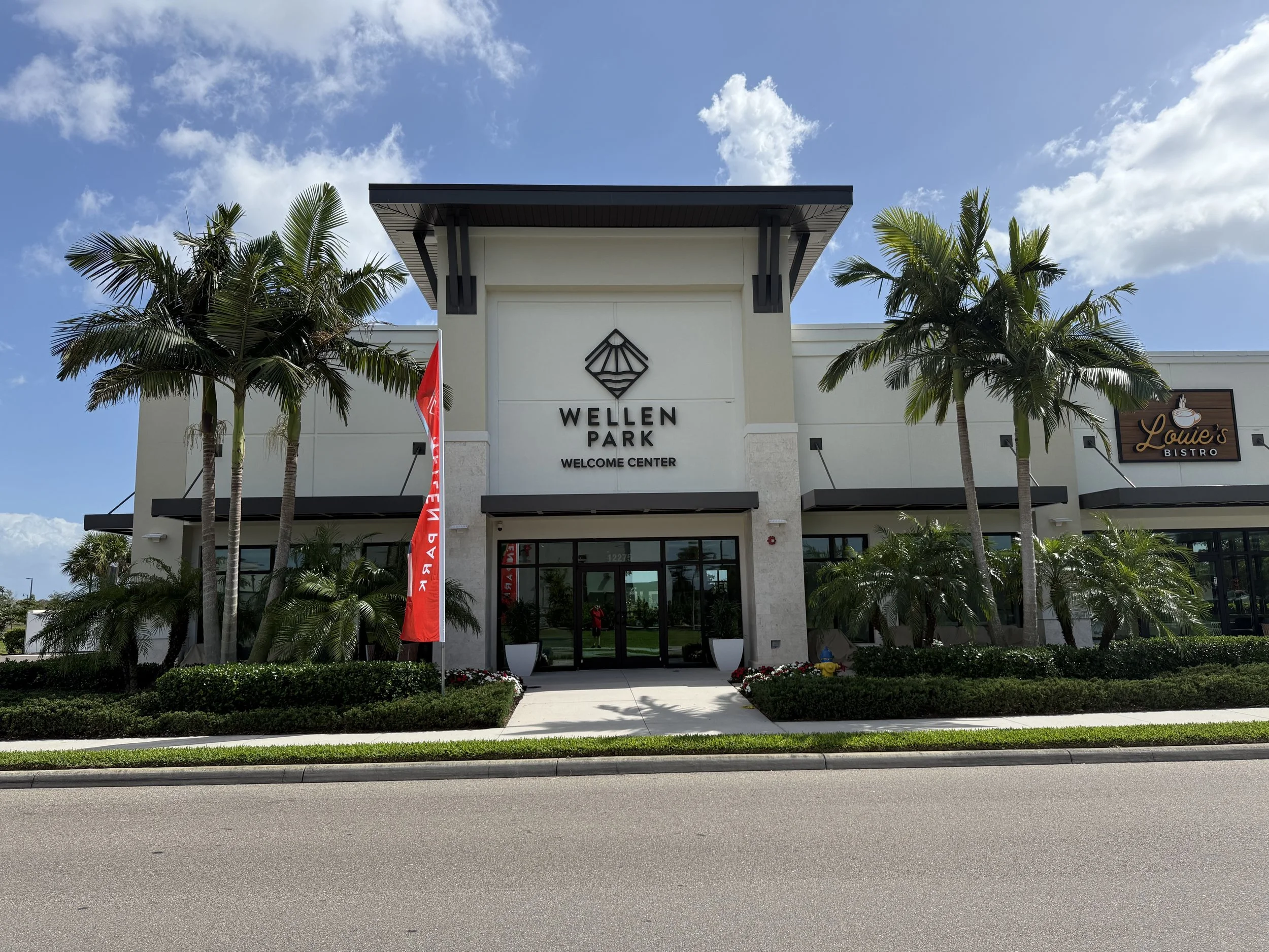 Front view of the Wellen Park Welcome Center building with palm trees, landscaping, and a bright blue sky.
