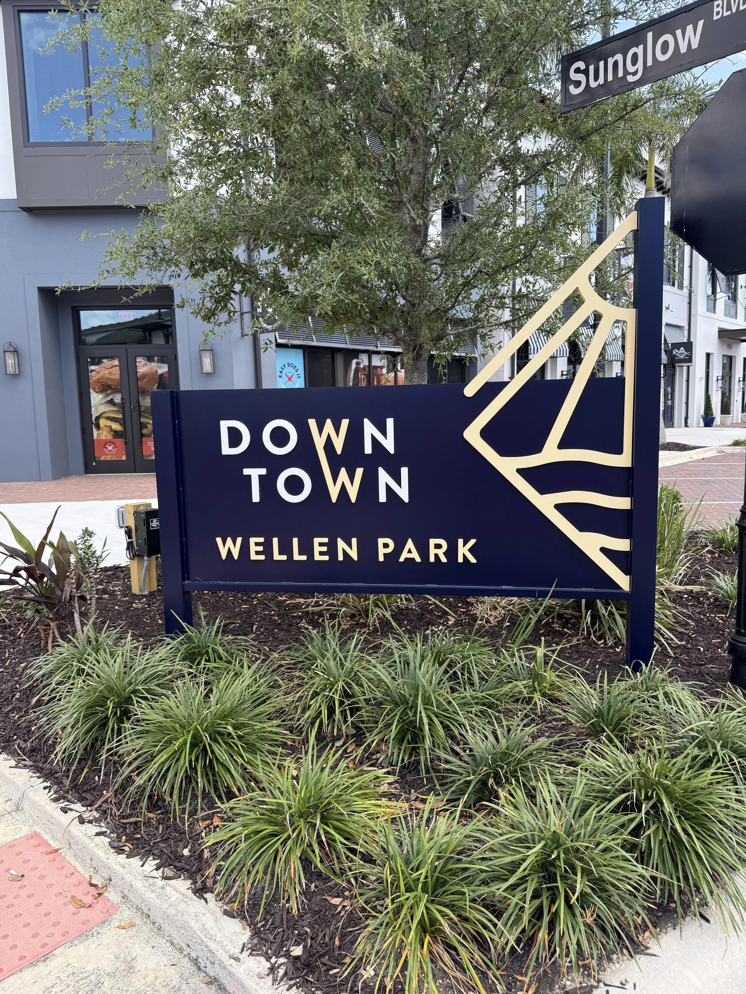 Street sign for Sullivan Boulevard, traffic light with red signal, plants and landscaping in a modern shopping or office area, building with large windows and a sign for Easy Dog.