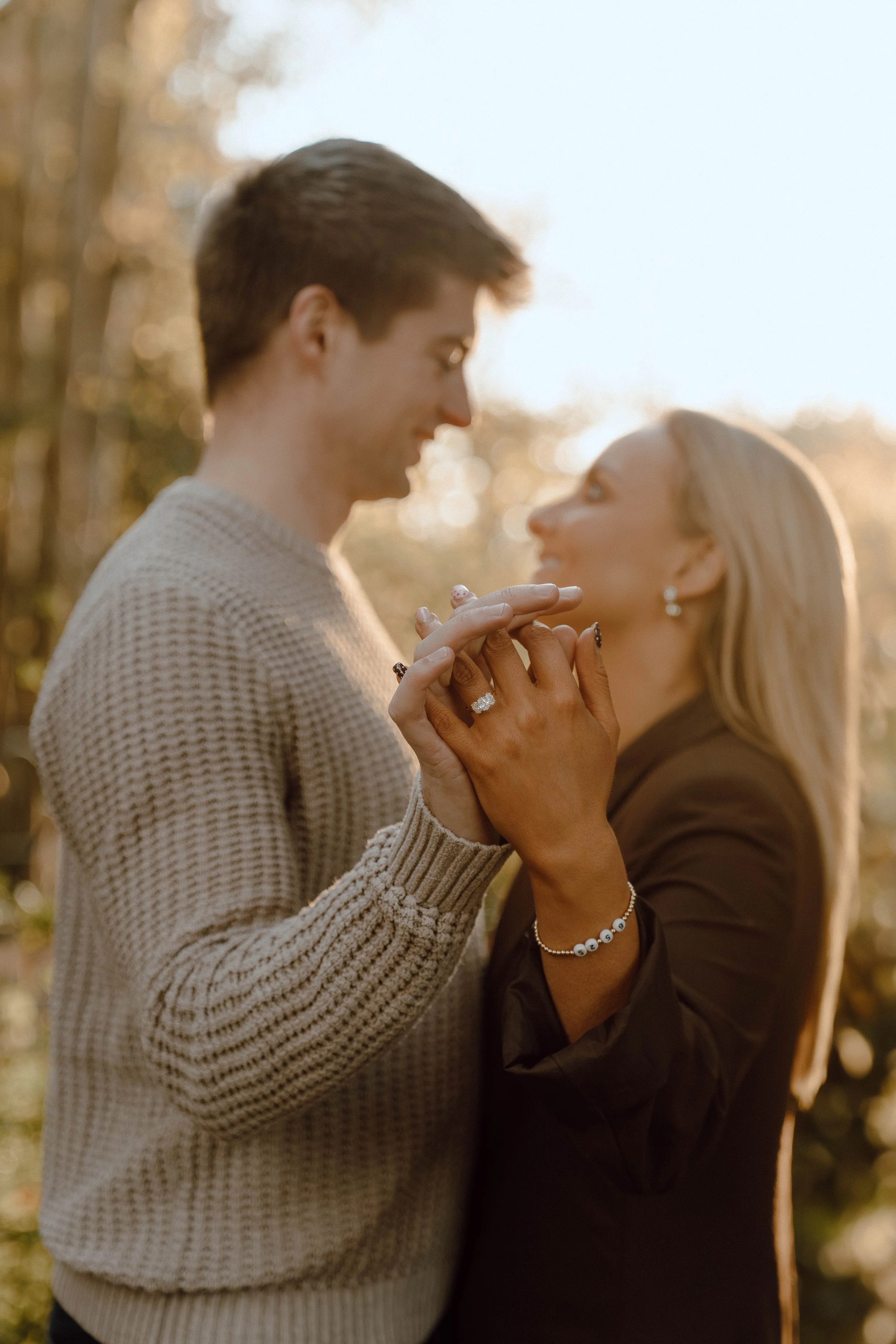 A couple holding hands and gazing at each other outdoors during golden hour.
