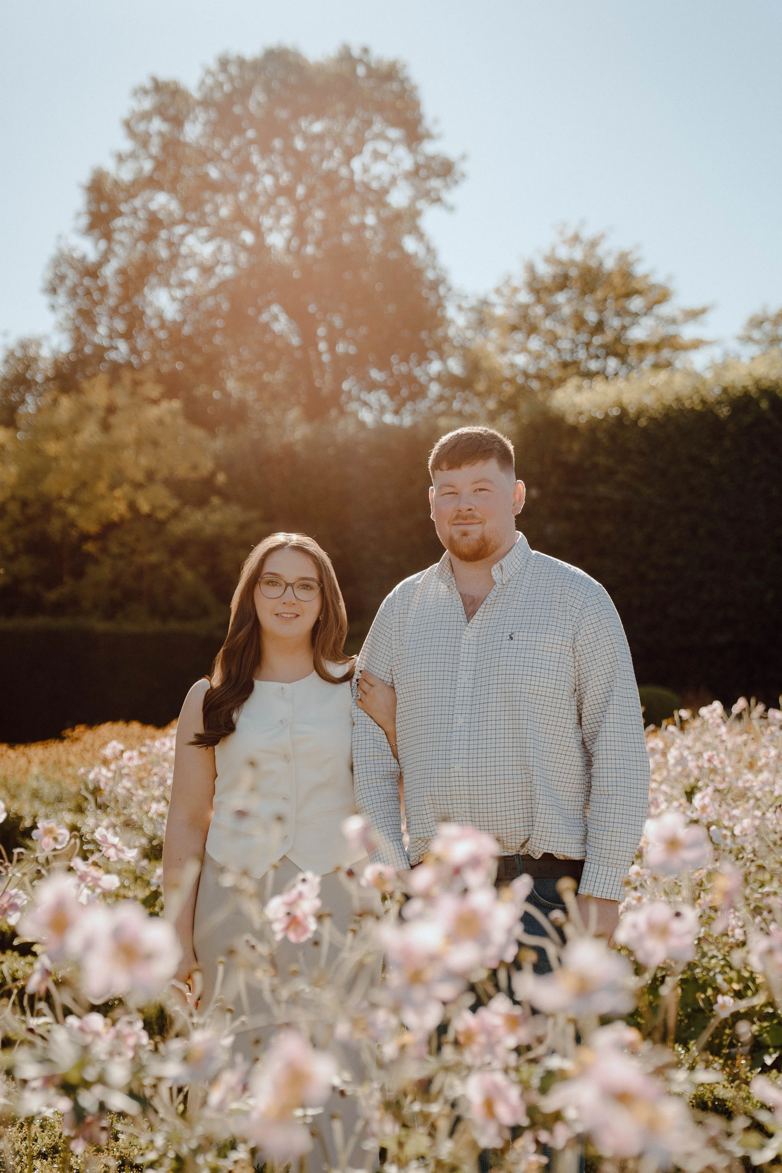 A young woman and man standing together in a flower field during golden hour sunlight.