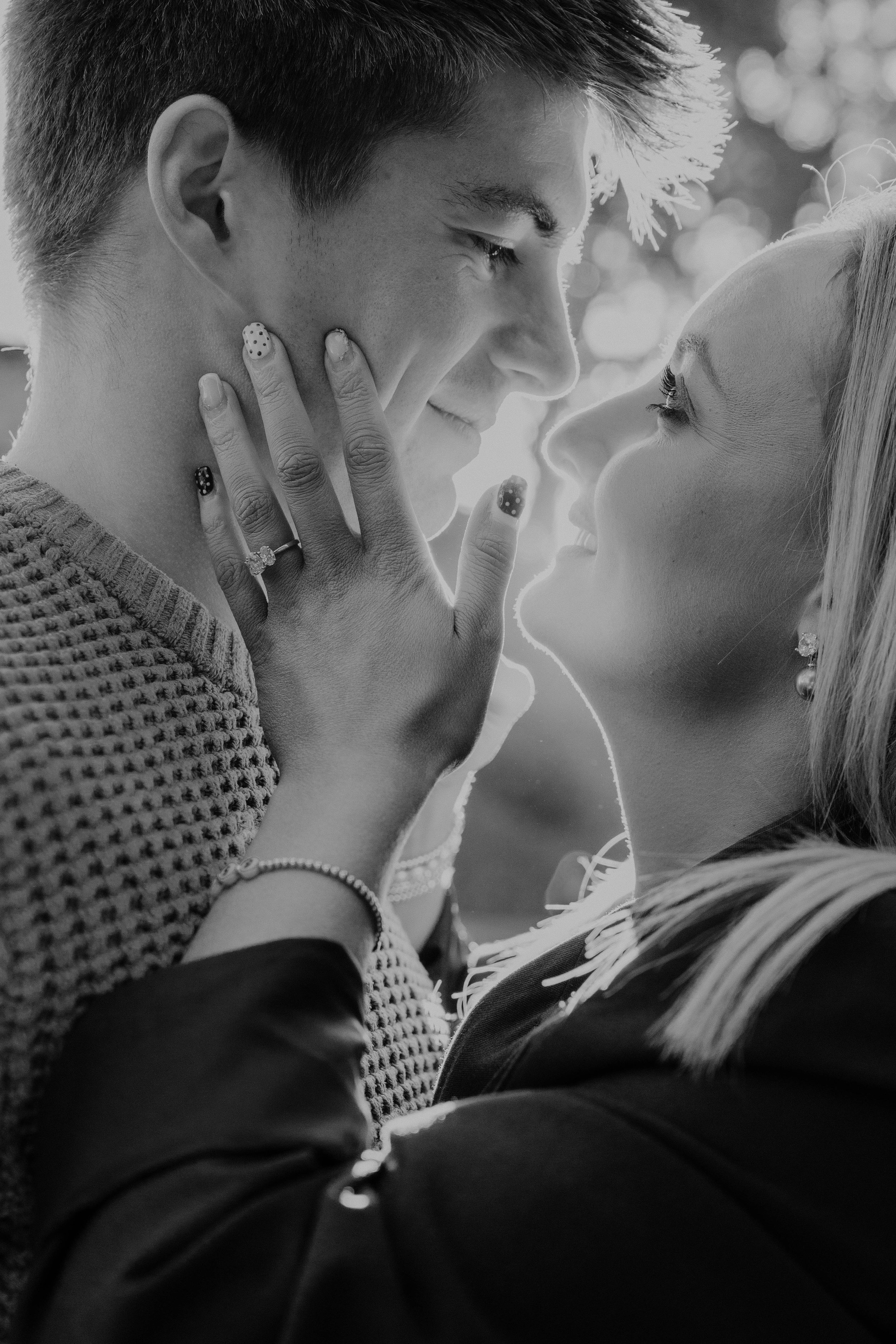 A young couple is looking into each other's eyes, with the woman touching the man's face. The photo is in black and white, capturing a romantic moment.