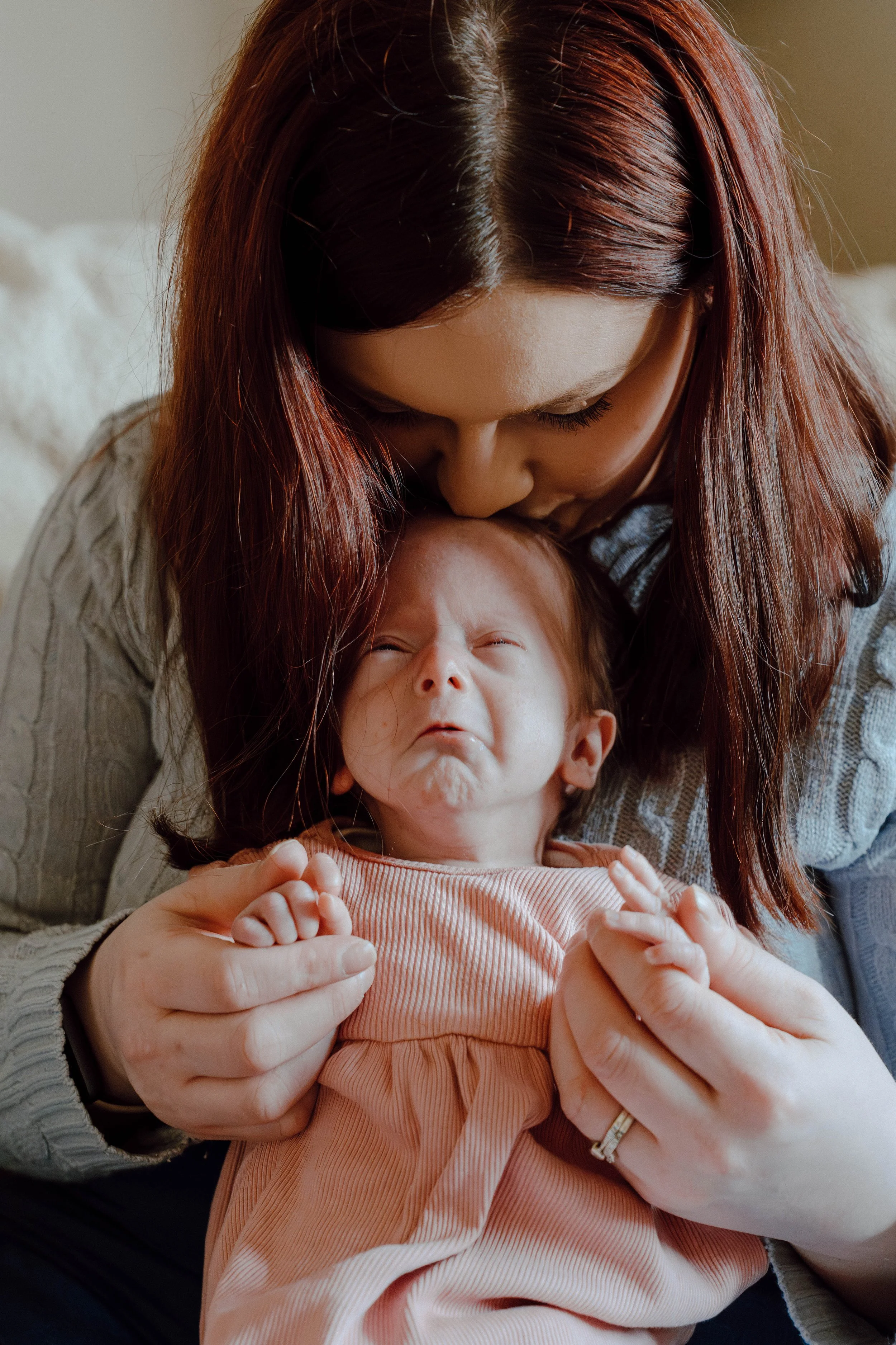 A woman with reddish-brown hair holding and comforting a crying baby.