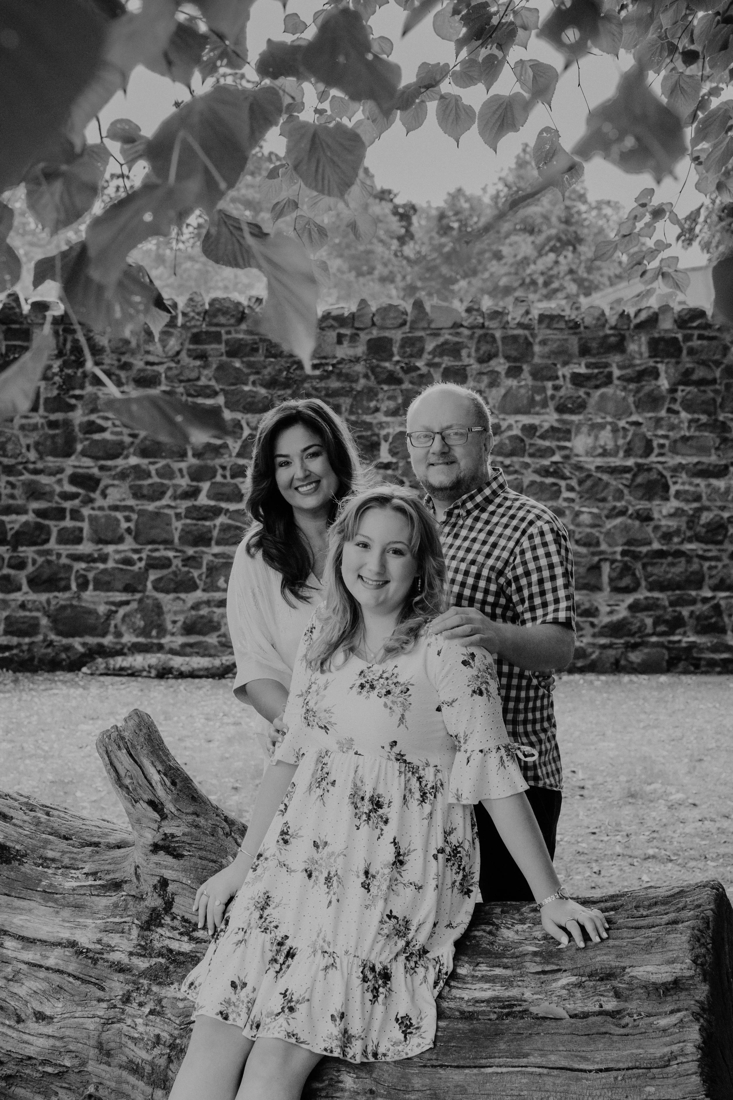 Family portrait outdoors with a woman, a man, and a girl in front of a stone wall, smiling, black and white photograph.
