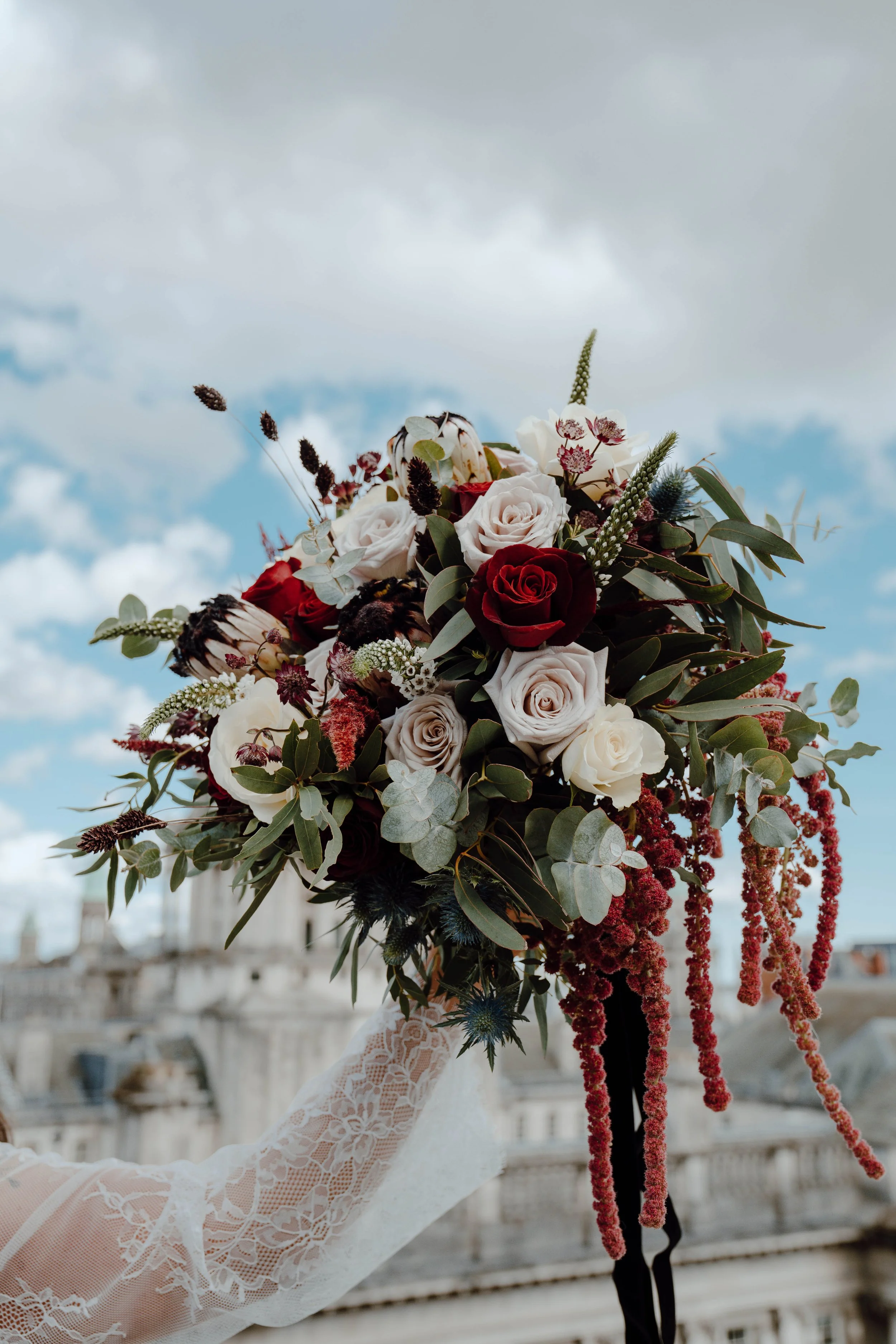 A person in a lace dress holding a bouquet of roses and mixed flowers against a cloudy sky background.