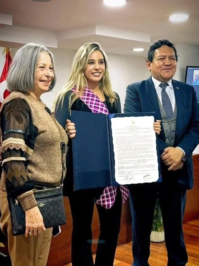 A woman is holding a signed document or certificate, flanked by two older adults, at an indoor event or ceremony.