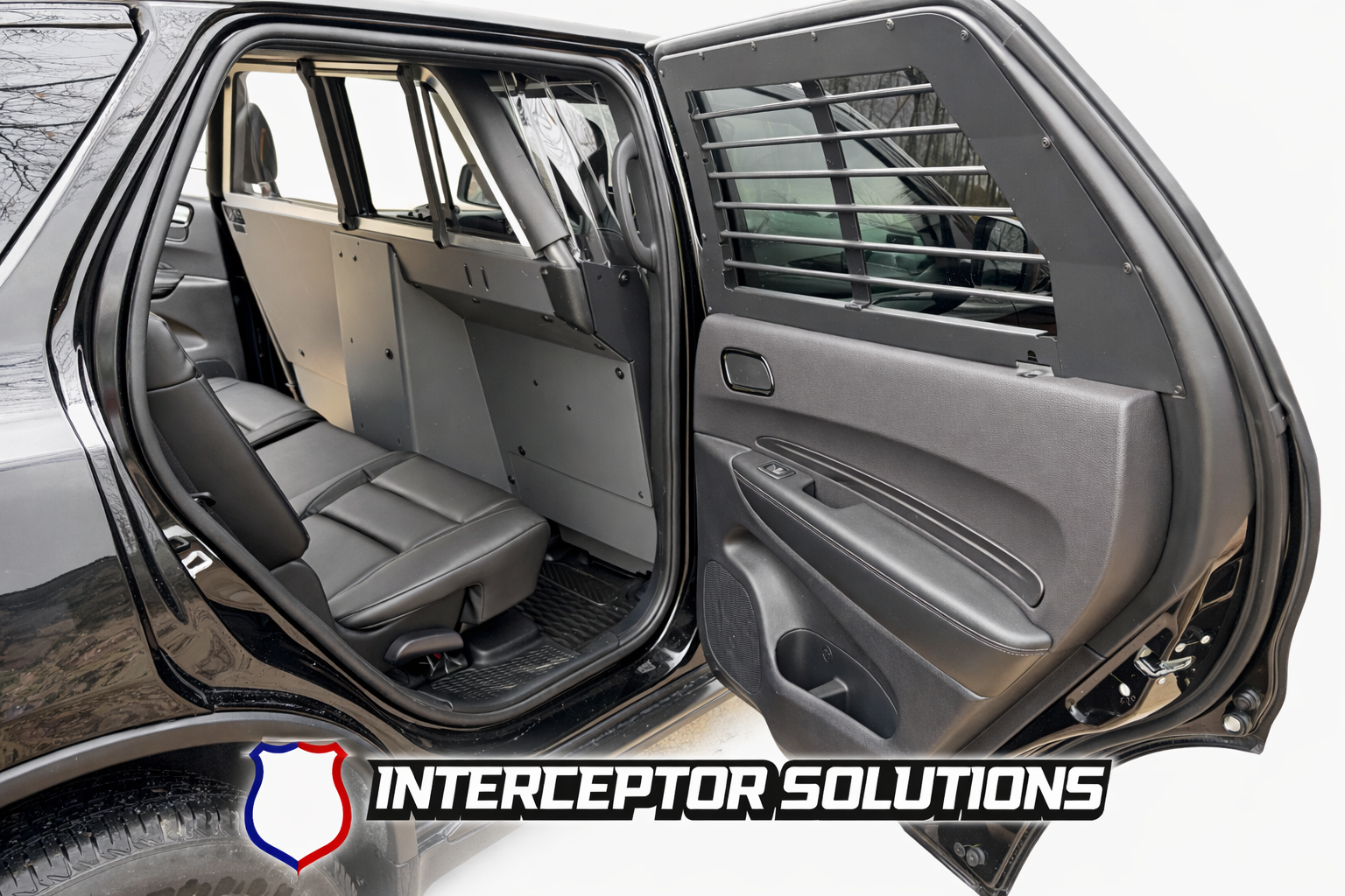 Interior of a black police or security vehicle with partition between the front and back seats, featuring a barred window on the rear passenger side door, and the logo of Interceptor Solutions at the bottom.