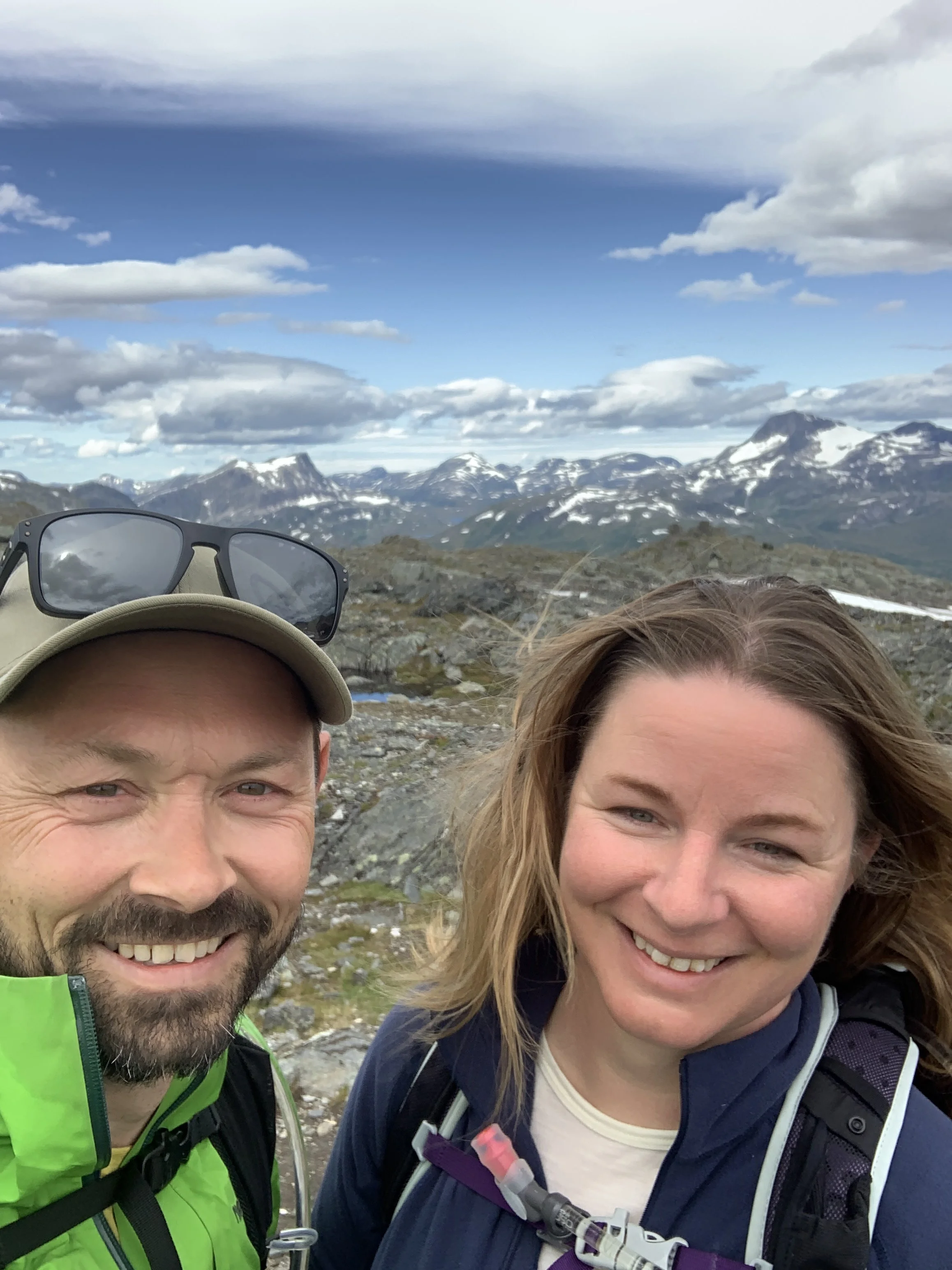A smiling man and woman hiking outdoors with mountainous landscape and snow-capped peaks in the background. Norwegian breeders of cocker spaniel