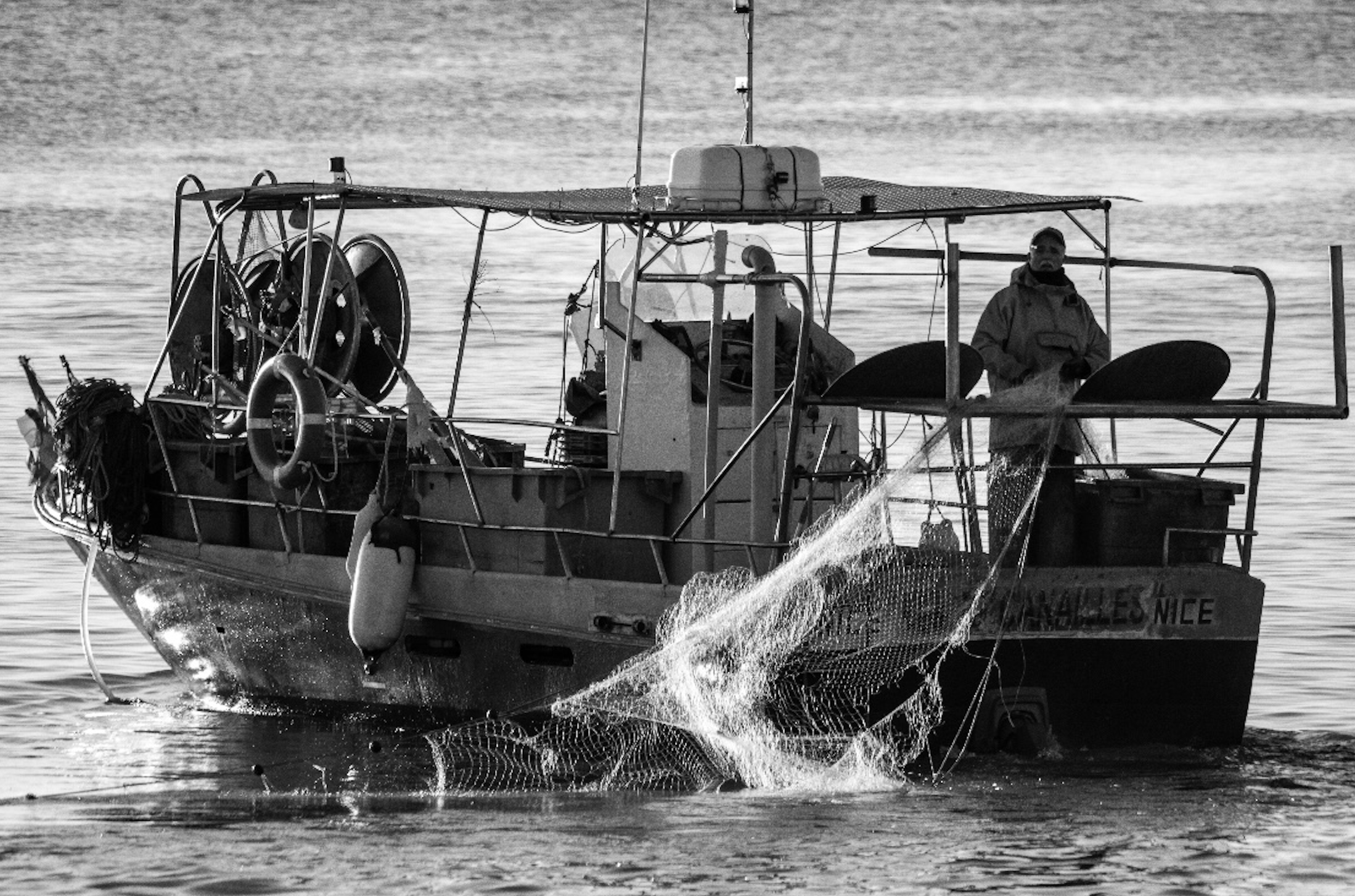 Bateau de pêche en mer au Cros-de-Cagnes, avec un filet relevé à l’arrière dans une scène en noir et blanc.