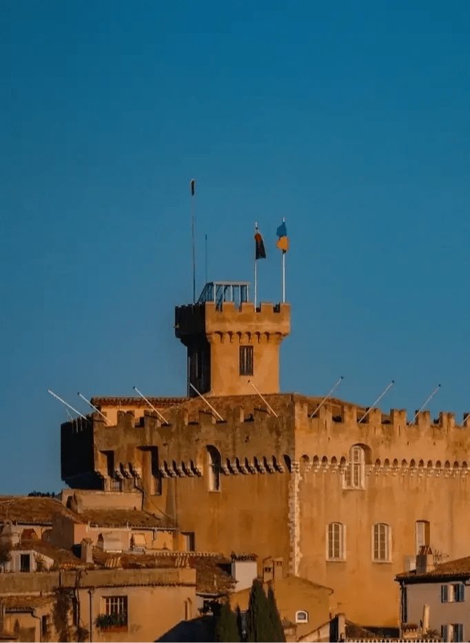 Tour du château du Haut-de-Cagnes éclairée par une lumière chaude, avec un ciel bleu en arrière-plan.