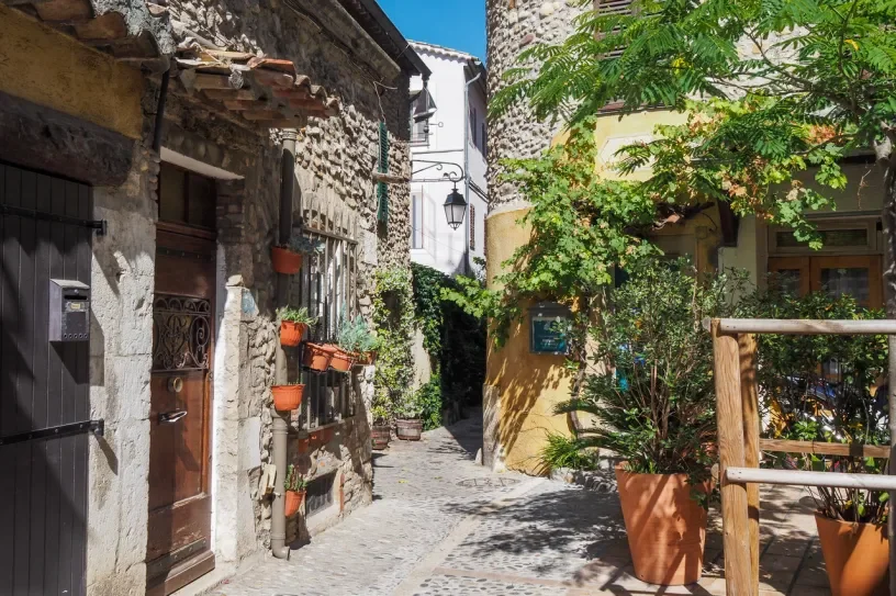 Ruelle pavée du Haut-de-Cagnes bordée de maisons anciennes en pierre, de volets colorés et de plantes en pots.