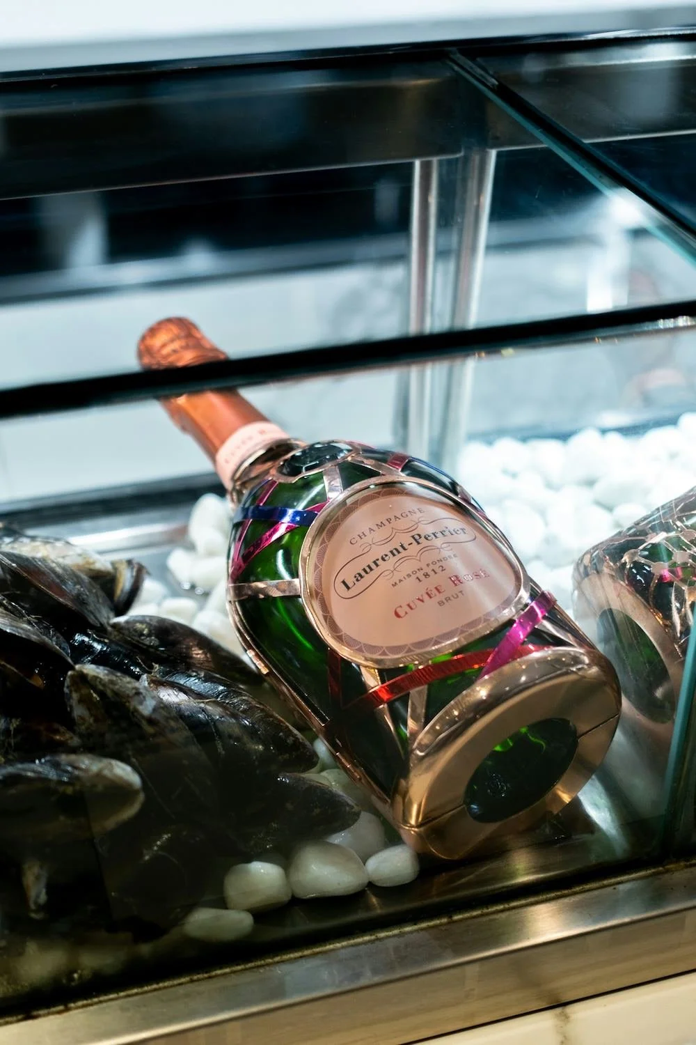 A bottle of Laurent-Perrier champagne and a pile of mussels on a bed of ice in a display case.