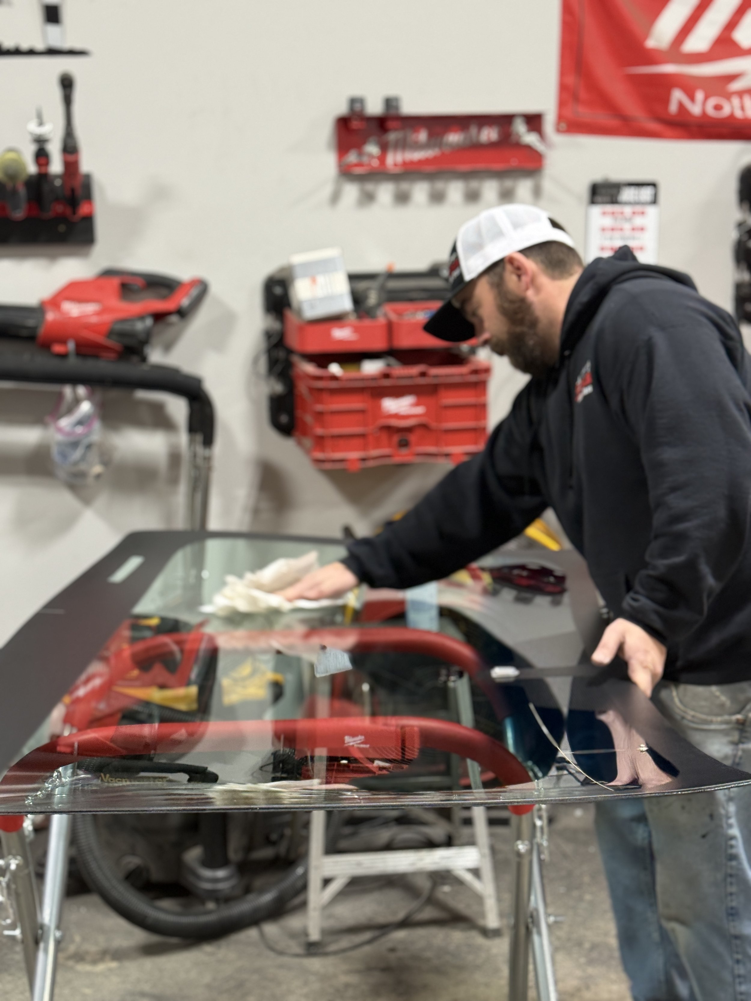 A person cleaning the windshield of a race car inside a workshop with tool shelves on the wall.